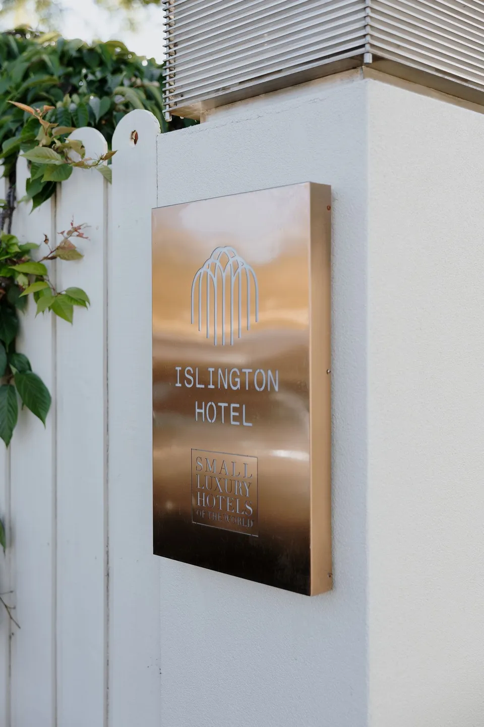 Islington Hotel’s brass entrance sign beside a white wall and climbing foliage, at Islington Hotel in South Hobart, Tasmania, Australia, for an Elopement Collective summer elopement. Photograph by George Bowden.