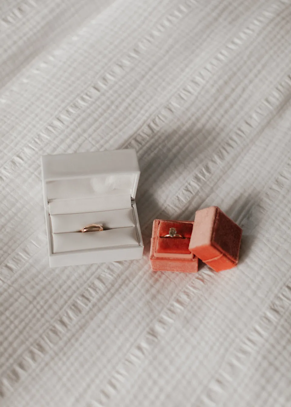 Wedding rings in white and orange velvet boxes on a textured white bedspread. At Fig Tree Villa in Ewingsdale, Byron Bay, for an Elopement Collective elopement. Photograph by Bulb Creative.
