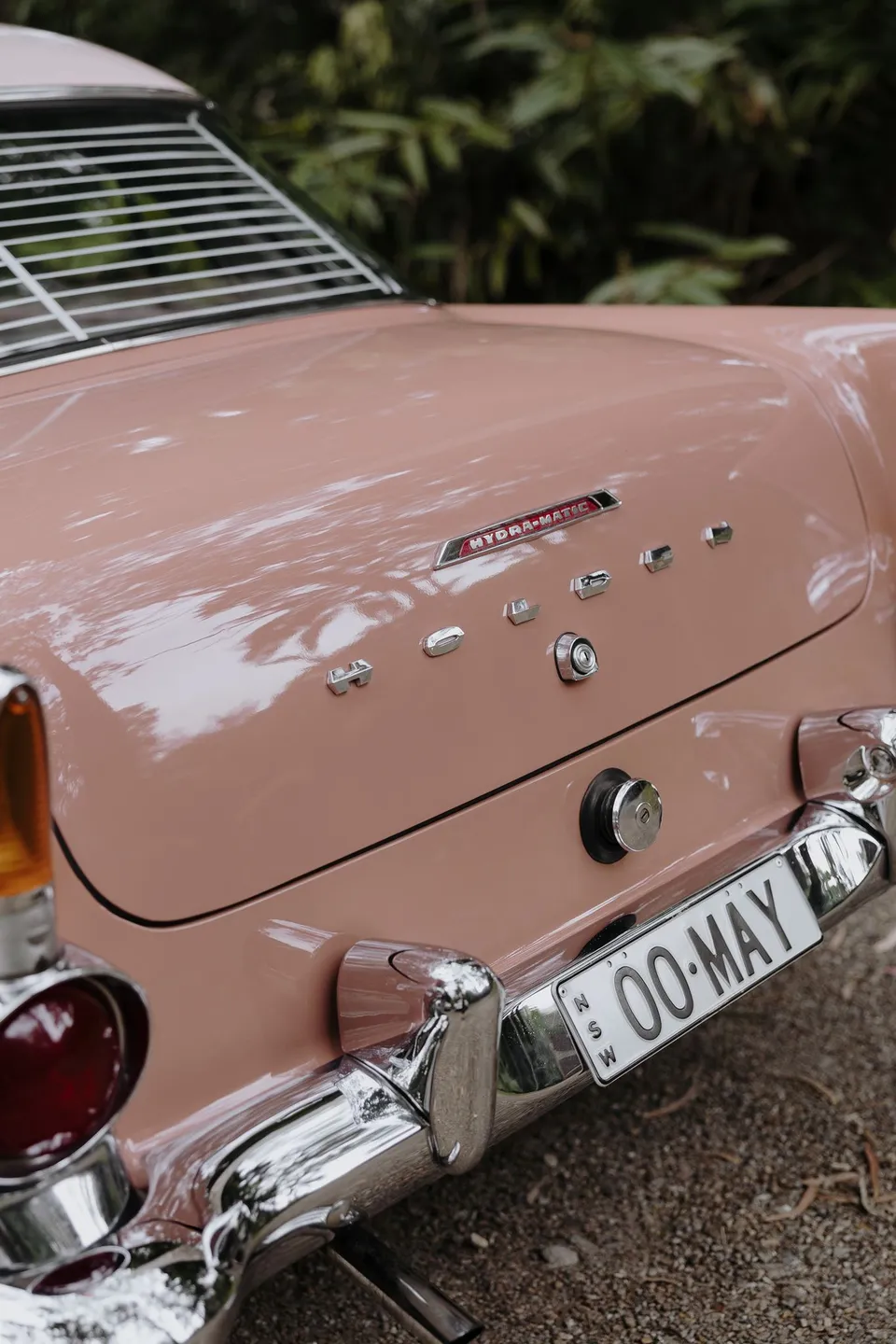 Close-up of the pink vintage Holden's chrome trim and boot badge from May The E.K. At Fig Tree Villa in Ewingsdale, Byron Bay, for an Elopement Collective elopement. Photograph by George Bowden.
