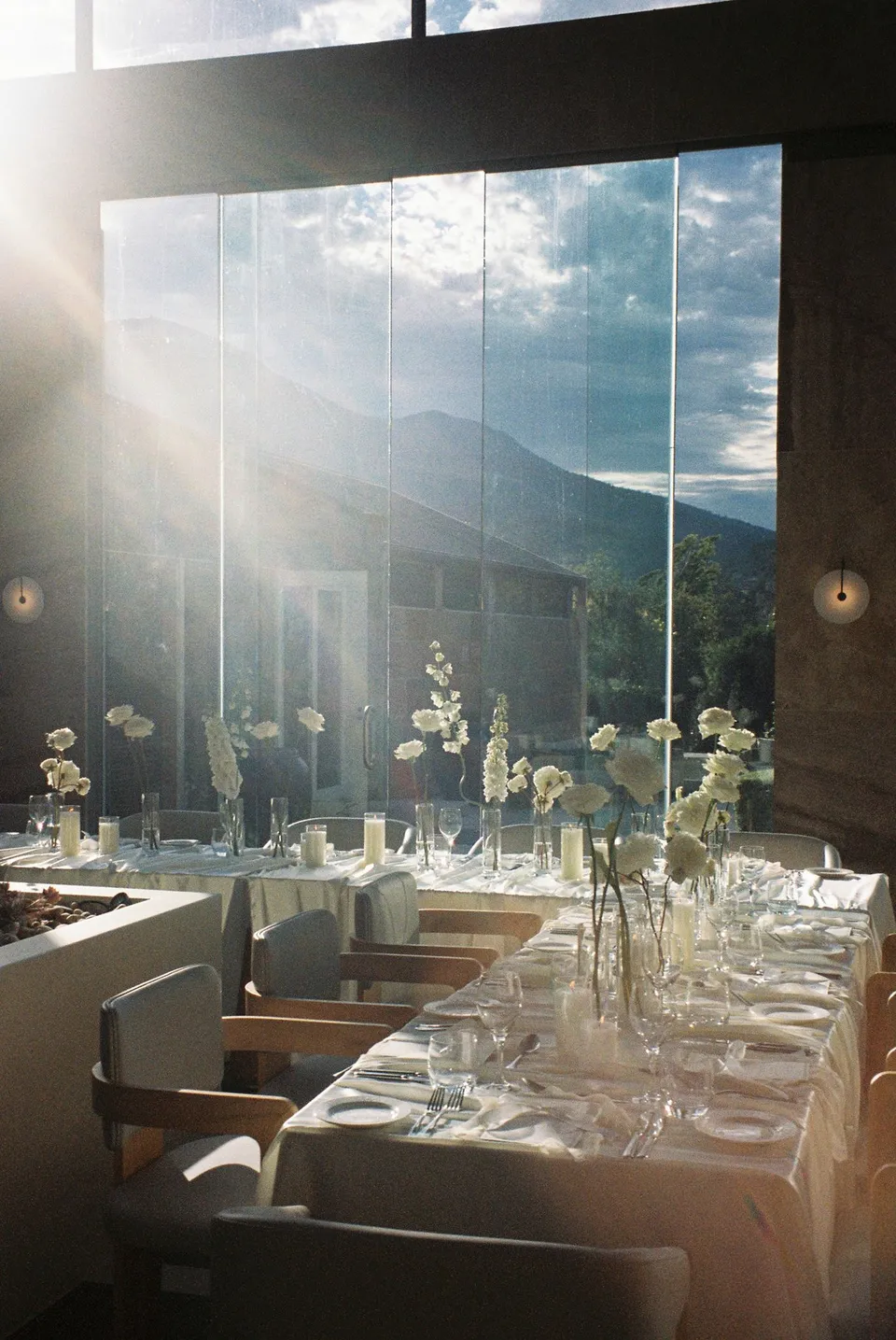 Sunlight falling across white flowers by The Romantics, candles and a reception table styled by Artaud & Co, with the mountain visible through the conservatory windows, at Islington Hotel in South Hobart, Tasmania, Australia, for an Elopement Collective summer elopement. Photograph by George Bowden.