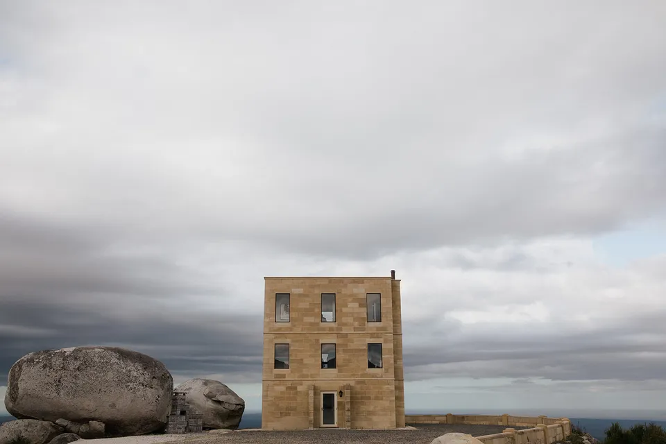 The Keep’s sandstone tower standing beside rounded granite boulders under a wide, clouded sky. At The Keep on Tasmania’s east coast, for an Elopement Collective elopement. Photograph by Jenna Agius.