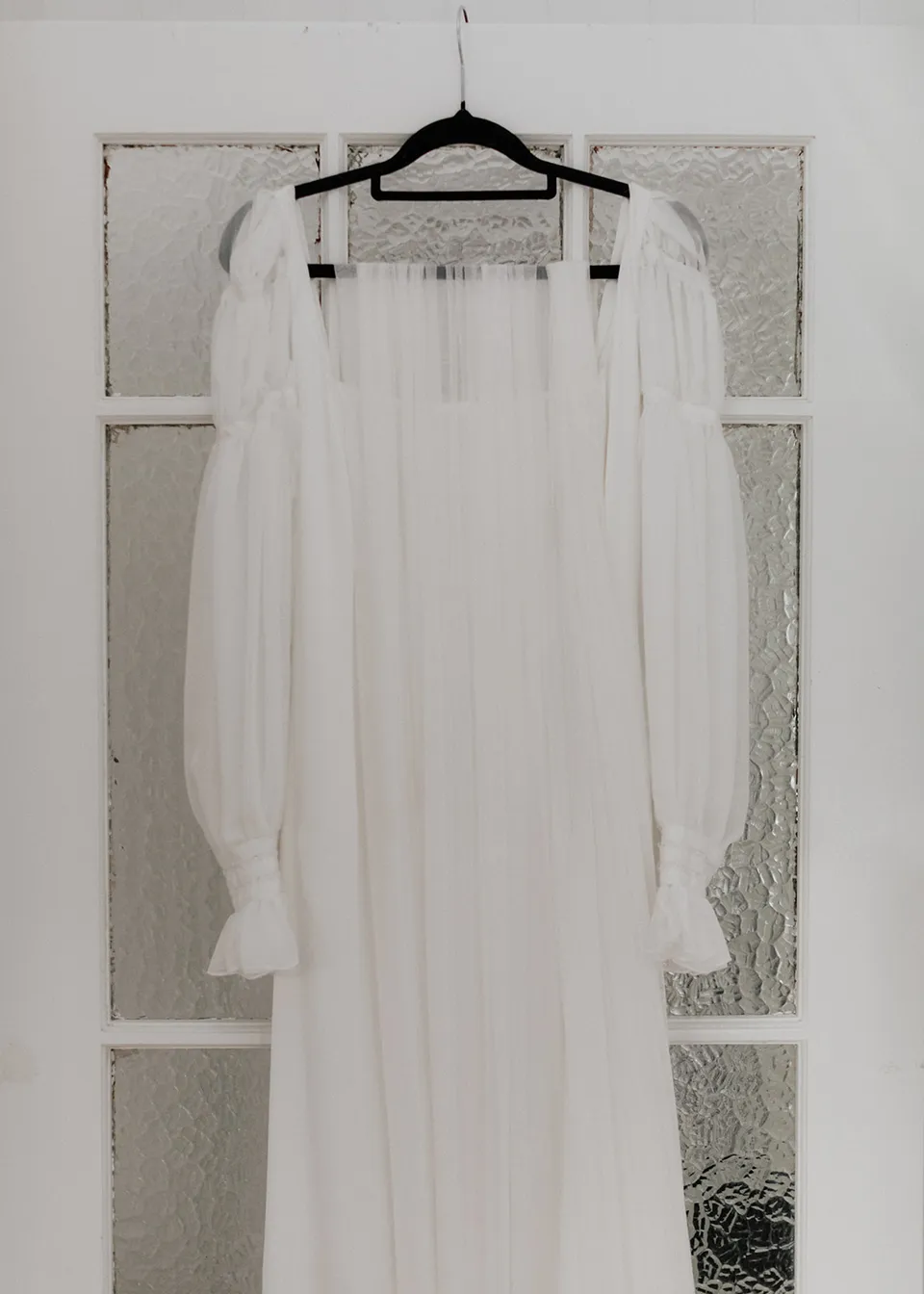 The bodice and sheer puff sleeves of Elyse's wedding dress against a white door. At Fig Tree Villa in Ewingsdale, Byron Bay, for an Elopement Collective elopement. Photograph by Bulb Creative.