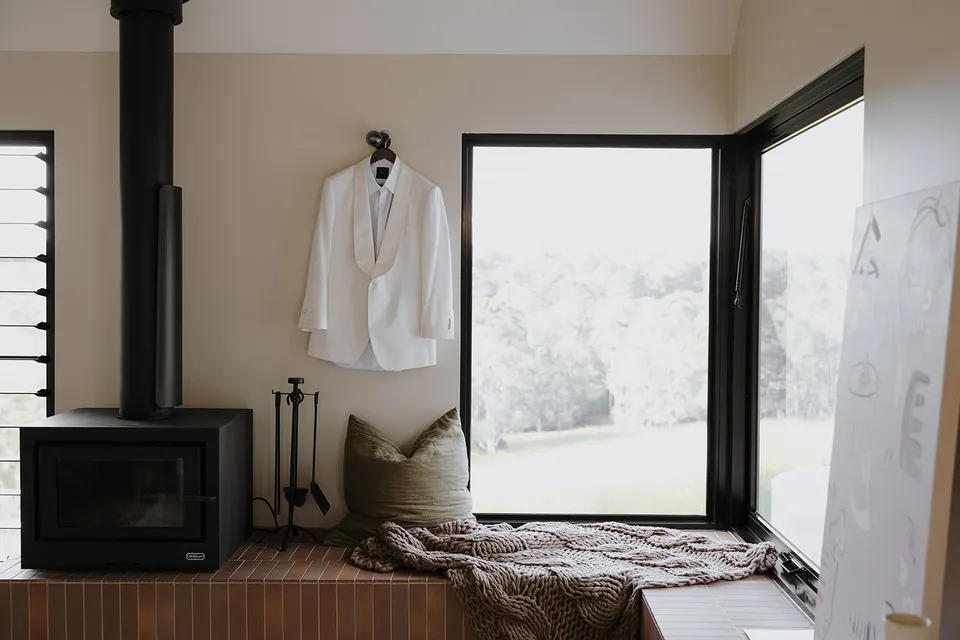Greg’s white dinner jacket hanging beside the cabin fireplace and an open window seat before an Elopement Collective elopement at Roundhill Retreat in Obi Obi, Sunshine Coast Hinterland.