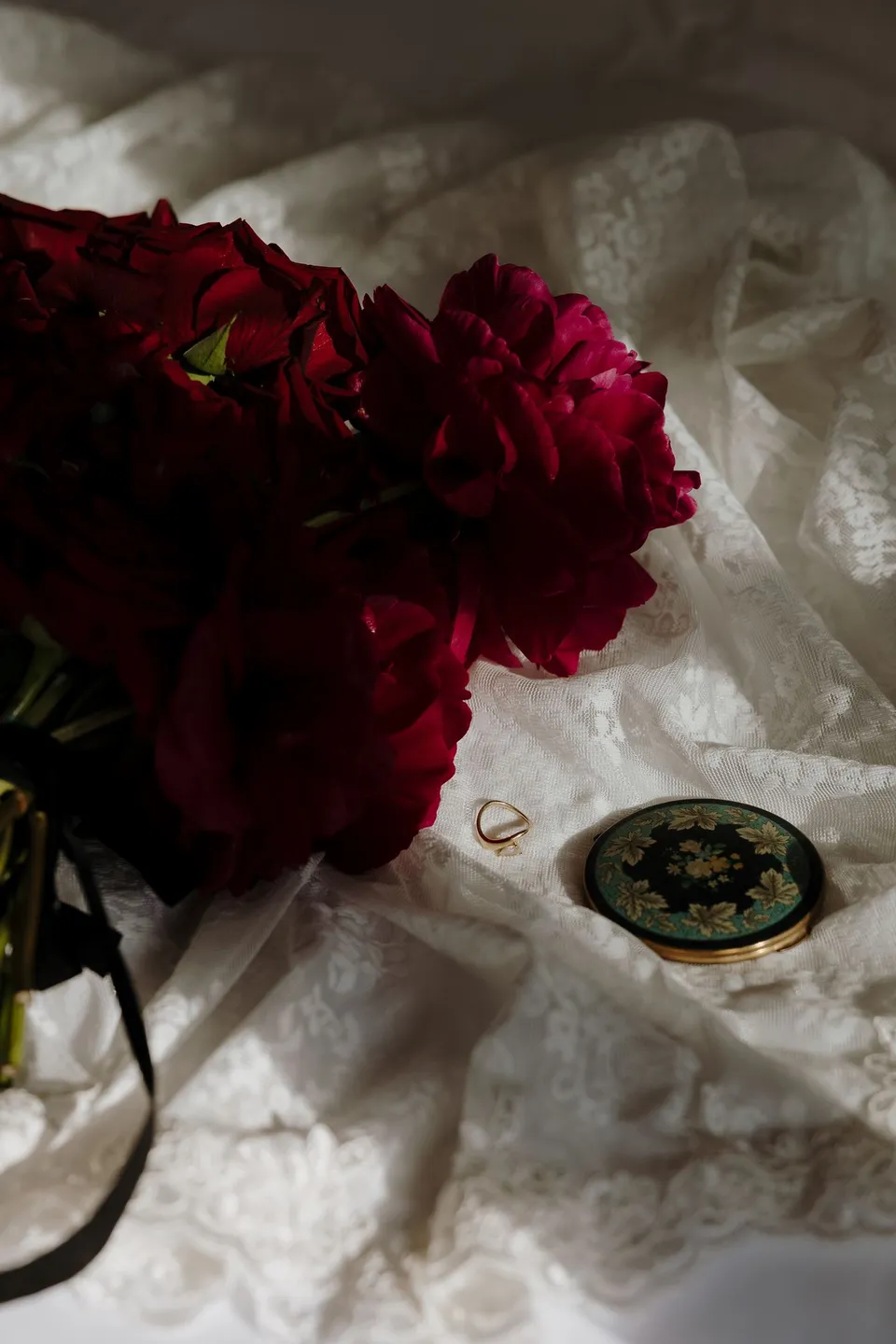 Deep red flowers by Ivy Bleu arranged with a gold ring, a floral compact and Kara’s lace veil, at Hotel Marignan Champs-Élysées in Paris, France, during an Elopement Collective elopement. Photograph by George Bowden.