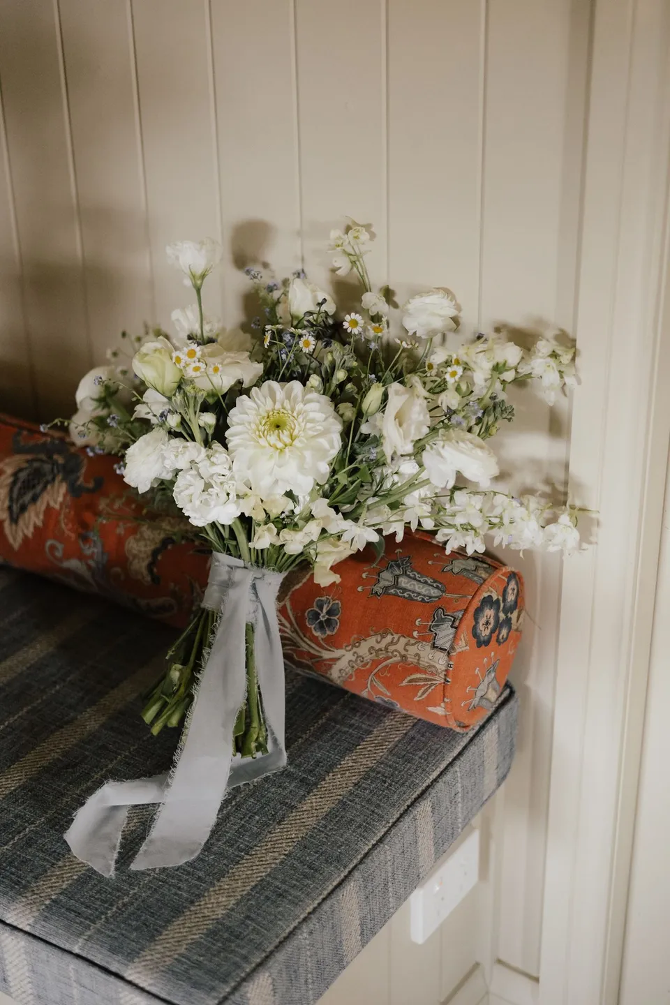 A white and green bouquet by Fifth Avenue Florist resting beside a cushion on a window seat. At Cudgera Creek in northern New South Wales, for an Elopement Collective elopement. Photograph by Bulb Creative.