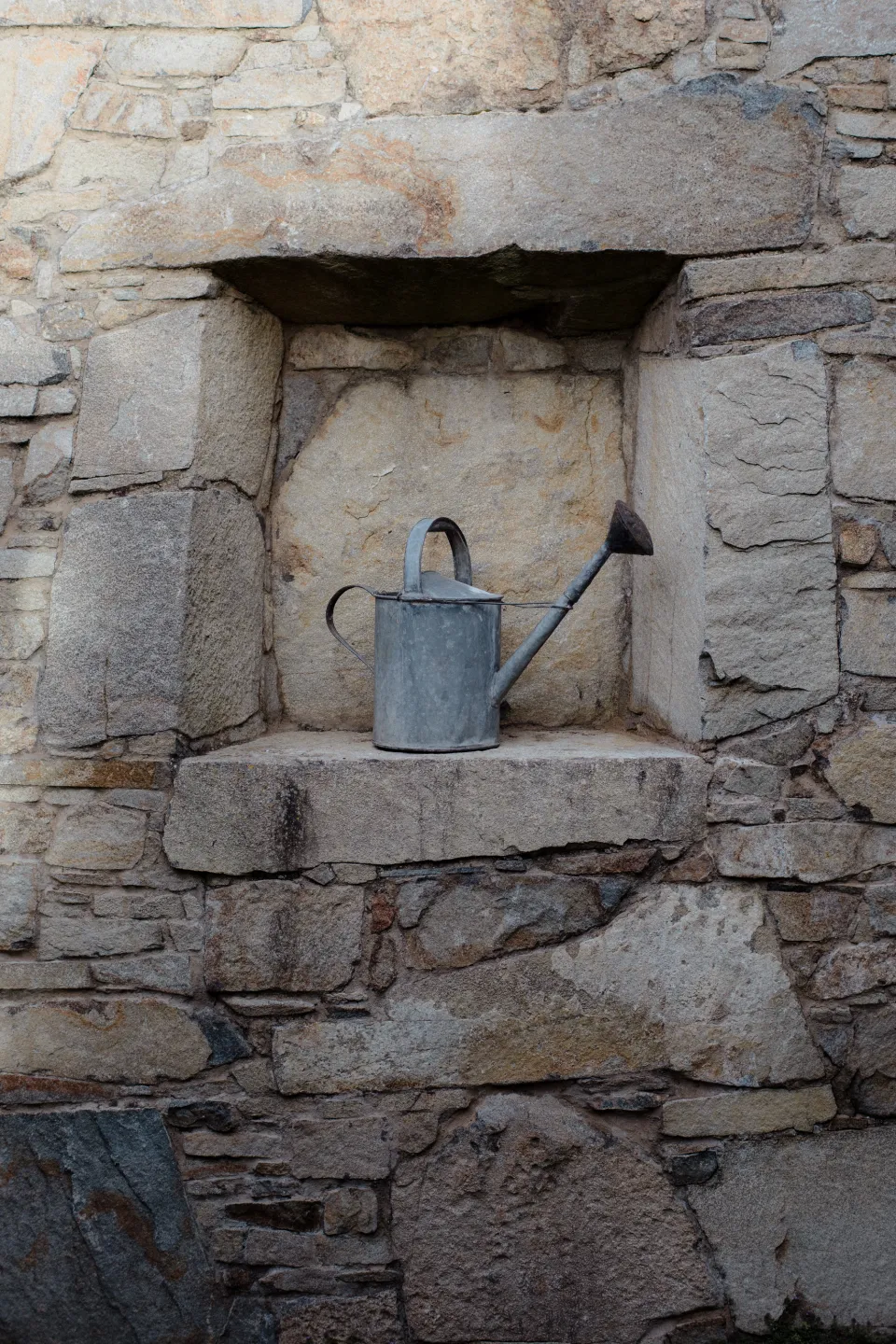 A metal watering can resting in a recess in a stone wall, at Thalia Haven on the East Coast of Tasmania, Australia, for an Elopement Collective elopement. Photograph by Joey Willis.