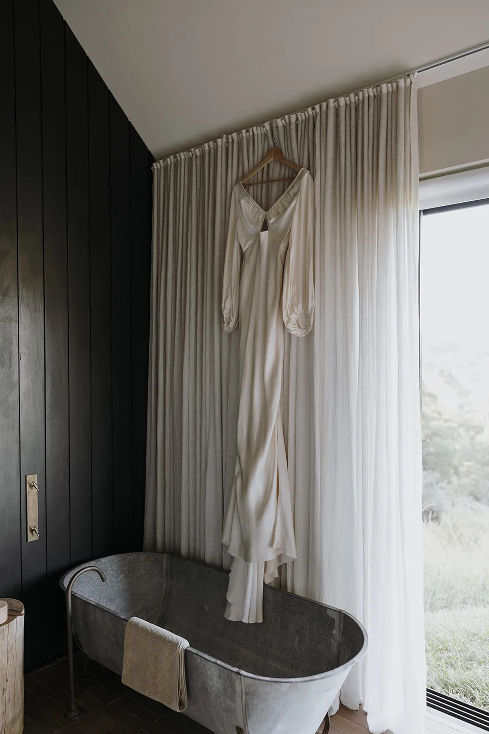 Gabrielle’s ivory dress hanging above a freestanding bath beside the cabin window before her Elopement Collective elopement at Roundhill Retreat in Obi Obi, Sunshine Coast Hinterland.