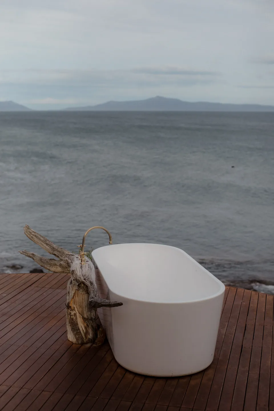 The white outdoor bathtub on a timber deck overlooking Great Oyster Bay, at Thalia Haven on the East Coast of Tasmania, Australia, for an Elopement Collective elopement. Photograph by Joey Willis.