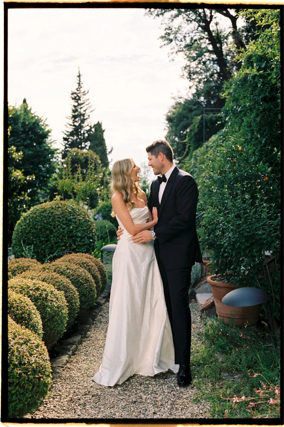 Holly and Matthew holding each other beside clipped garden shrubs, at Villa San Michele in Fiesole above Florence, Tuscany, Italy, for an Elopement Collective elopement. Film photograph by Khara from House of Lucie.