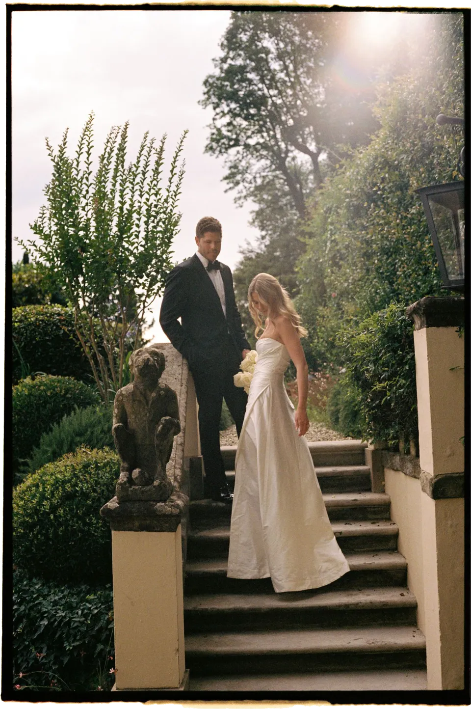 Holly and Matthew standing on garden steps beside a stone statue, at Villa San Michele in Fiesole above Florence, Tuscany, Italy, for an Elopement Collective elopement. Film photograph by Khara from House of Lucie.