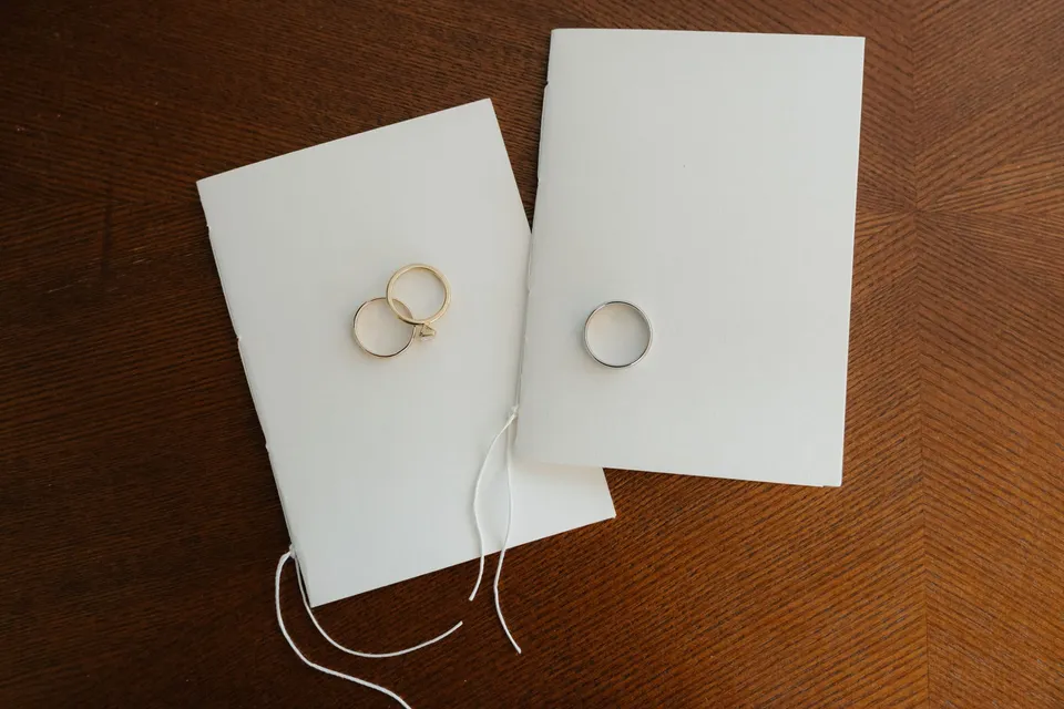 Wedding rings resting on two white vow books on a timber table, at their alpine Airbnb in Ben Lomond, Queenstown, New Zealand, for an Elopement Collective Queenstown elopement. Photograph by Bulb Creative.