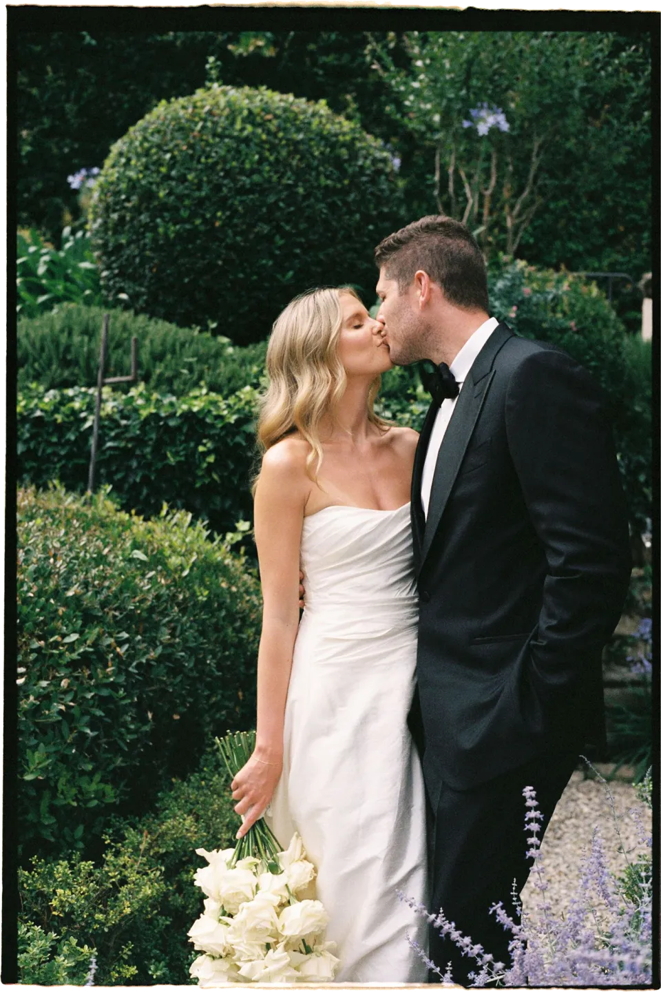 Holly and Matthew kissing beside the garden hedges, with Holly holding her white bouquet by Le Francesche Flower Designers, at Villa San Michele in Fiesole above Florence, Tuscany, Italy, for an Elopement Collective elopement. Film photograph by Khara from House of Lucie.