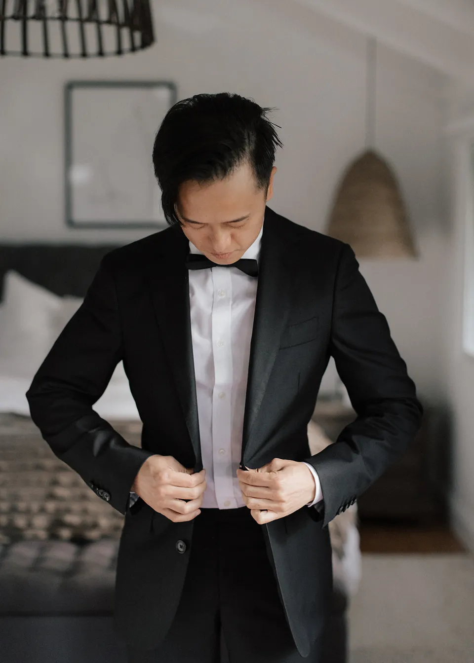 Jonathan looking down as he buttons his black suit jacket. At Fig Tree Villa in Ewingsdale, Byron Bay, for an Elopement Collective elopement. Photograph by Bulb Creative.