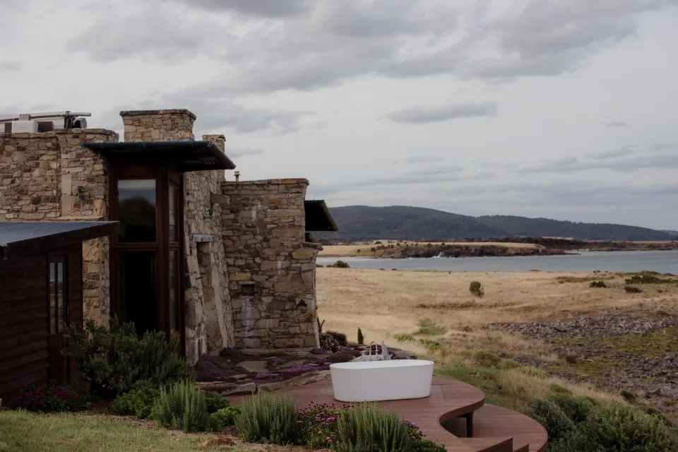 Stone buildings and the outdoor bath above the coastal meadow, at Thalia Haven on the East Coast of Tasmania, Australia, for an Elopement Collective elopement. Photograph by Joey Willis.