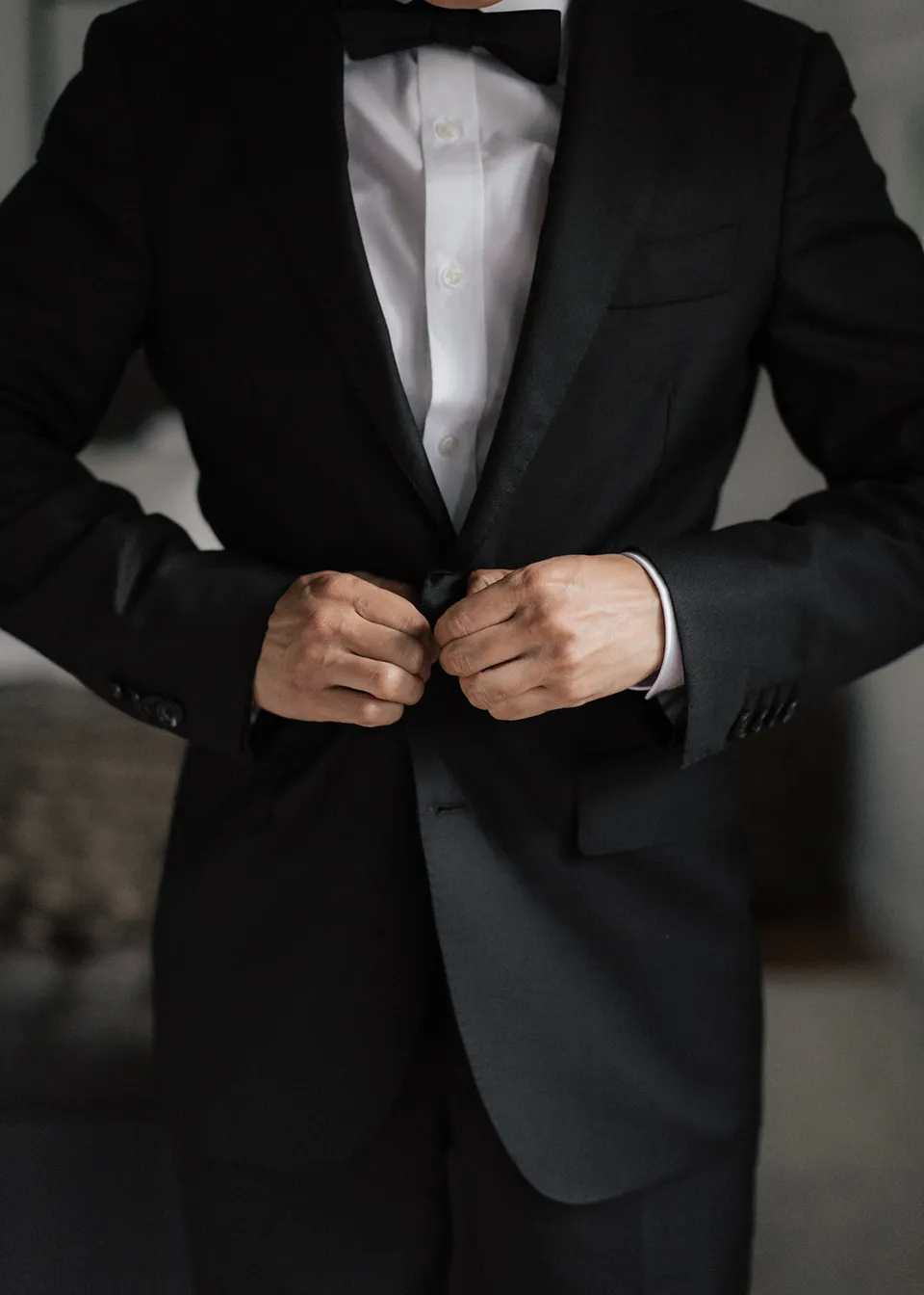 Close-up of Jonathan fastening his suit jacket beneath a black bow tie. At Fig Tree Villa in Ewingsdale, Byron Bay, for an Elopement Collective elopement. Photograph by Bulb Creative.