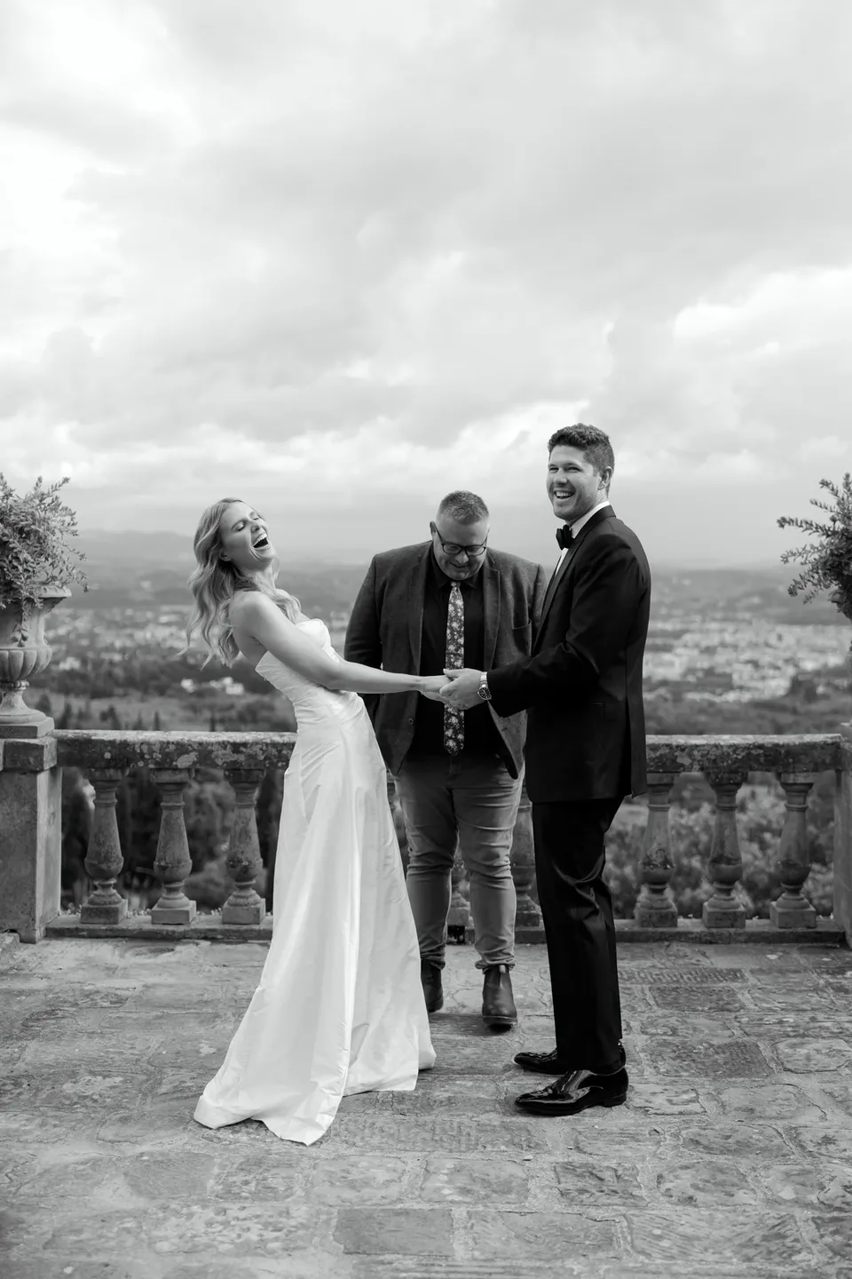 Black-and-white photograph of Josh Withers leading Holly and Matthew’s ceremony beside the stone terrace balustrade, at Villa San Michele in Fiesole above Florence, Tuscany, Italy, for an Elopement Collective elopement. Digital photograph by Khara from House of Lucie.