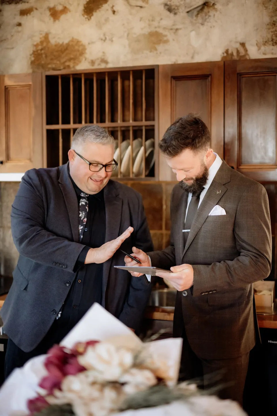 Celebrant Josh Withers and Russell smiling over a booklet inside the stone cottage. At Piermont Retreat on Tasmania’s east coast, for an Elopement Collective elopement. Photograph by Omar of By The Wilde.