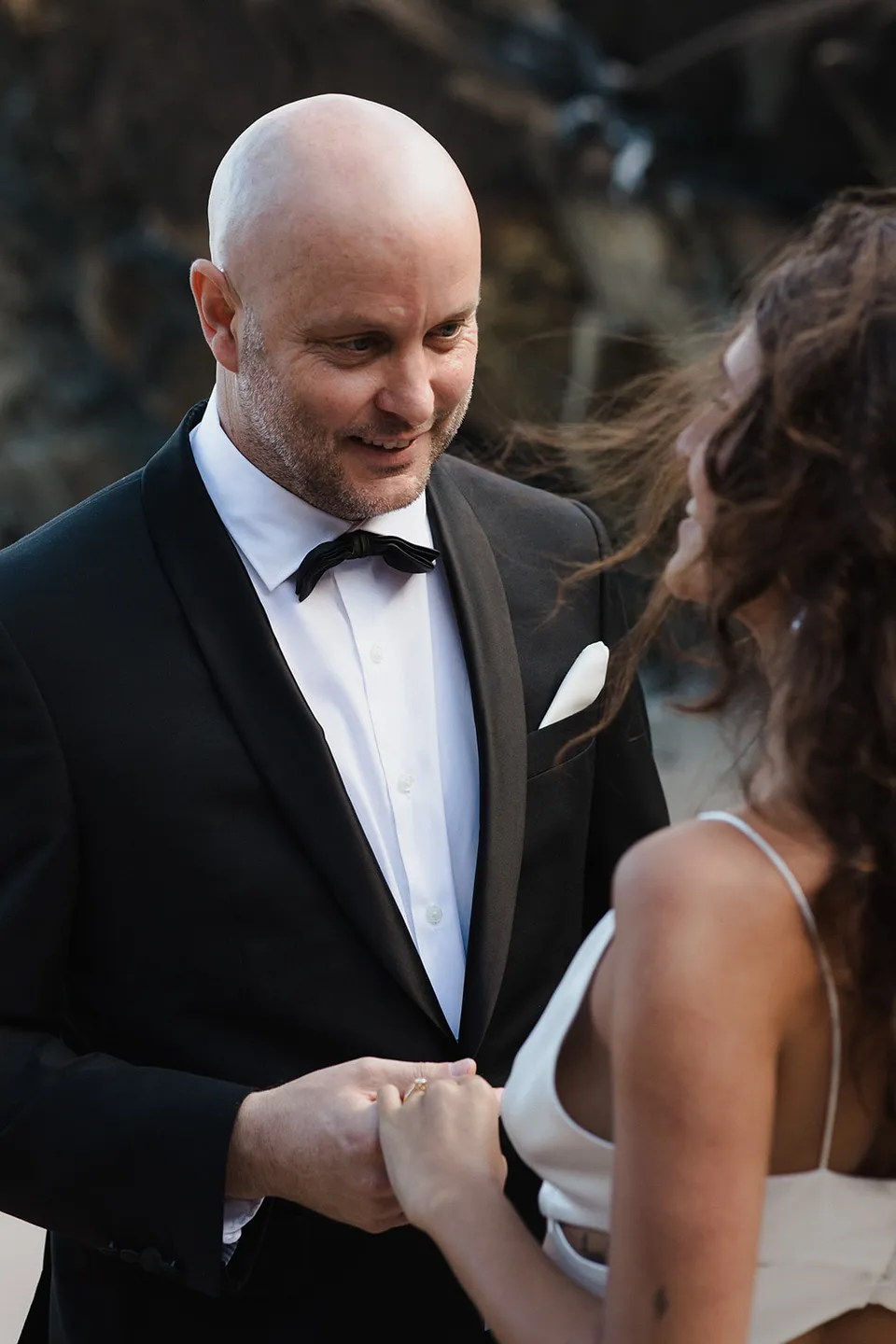 Dane smiling at Rachel during their beach ceremony. At Whites Beach, Broken Head, near Byron Bay, for an Elopement Collective elopement. Photograph by Jason Lucas.