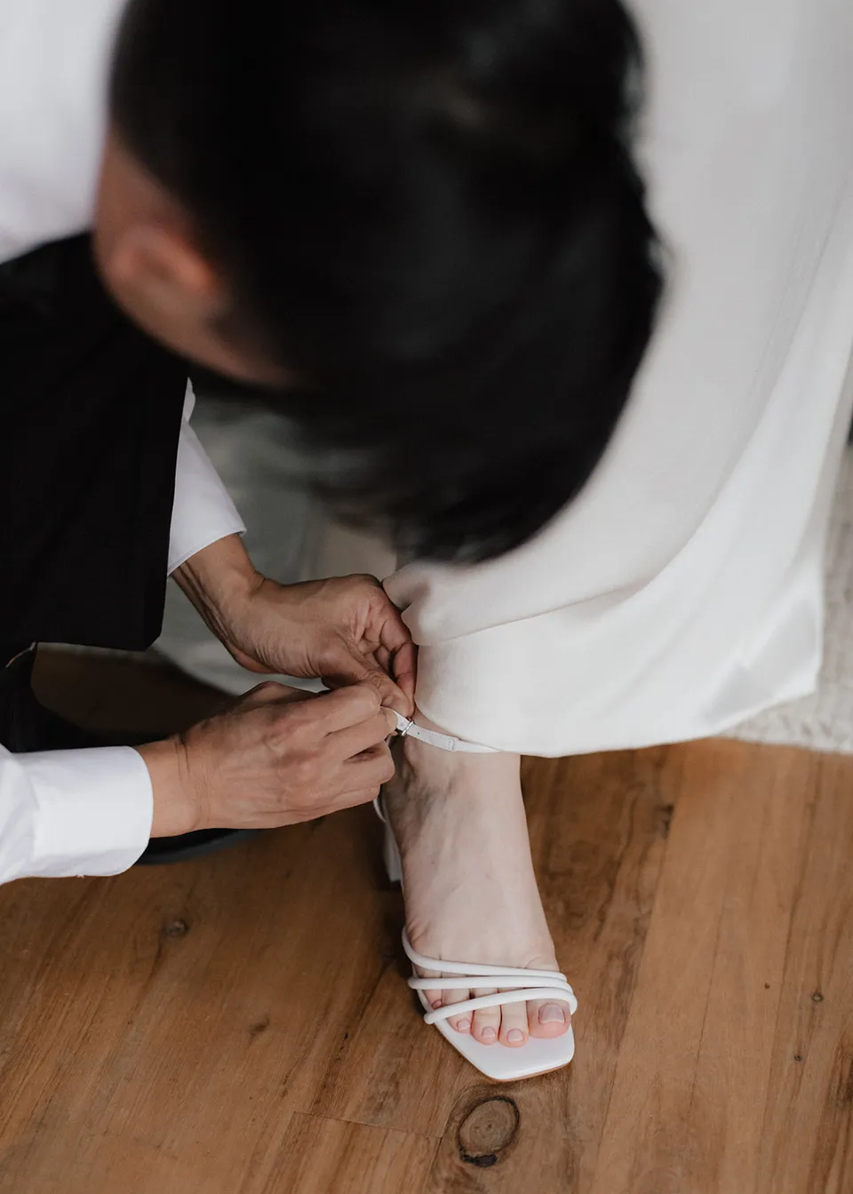 Overhead detail of Jonathan fastening the strap of Elyse's wedding shoe. At Fig Tree Villa in Ewingsdale, Byron Bay, for an Elopement Collective elopement. Photograph by Bulb Creative.