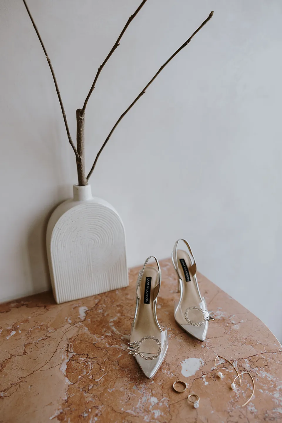 Gabrielle’s pointed slingback heels and jewellery on a stone table beside a white vase for an Elopement Collective elopement at Roundhill Retreat in Obi Obi, Sunshine Coast Hinterland.