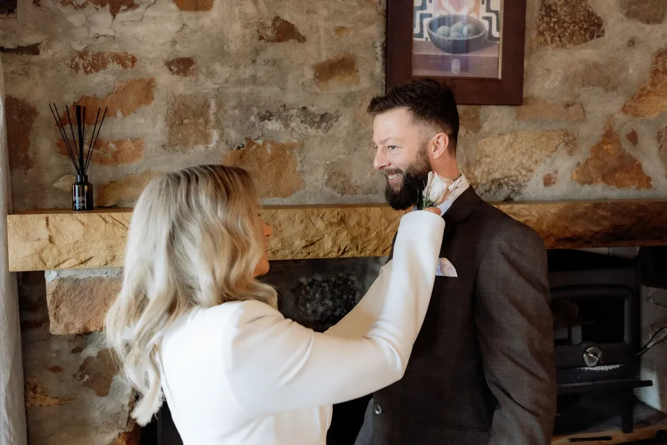 Kaitlyn adjusting Russell’s tie in front of the cottage’s stone fireplace. At Piermont Retreat on Tasmania’s east coast, for an Elopement Collective elopement. Photograph by Omar of By The Wilde.