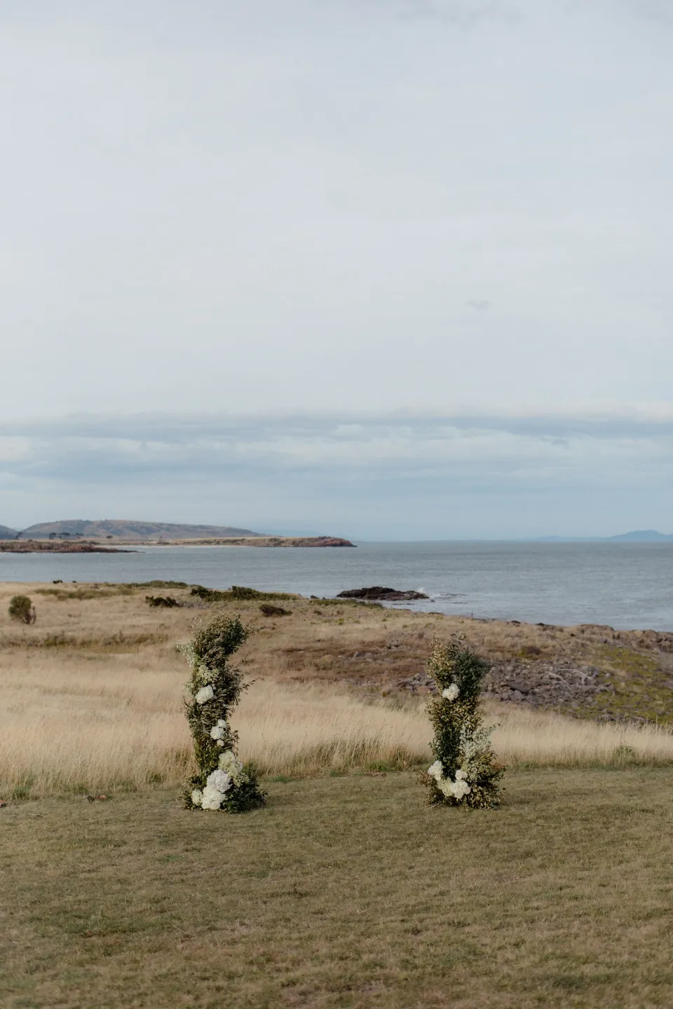 Two ceremony flower arrangements by The Romantics on the lawn above the bay, at Thalia Haven on the East Coast of Tasmania, Australia, for an Elopement Collective elopement. Photograph by Joey Willis.