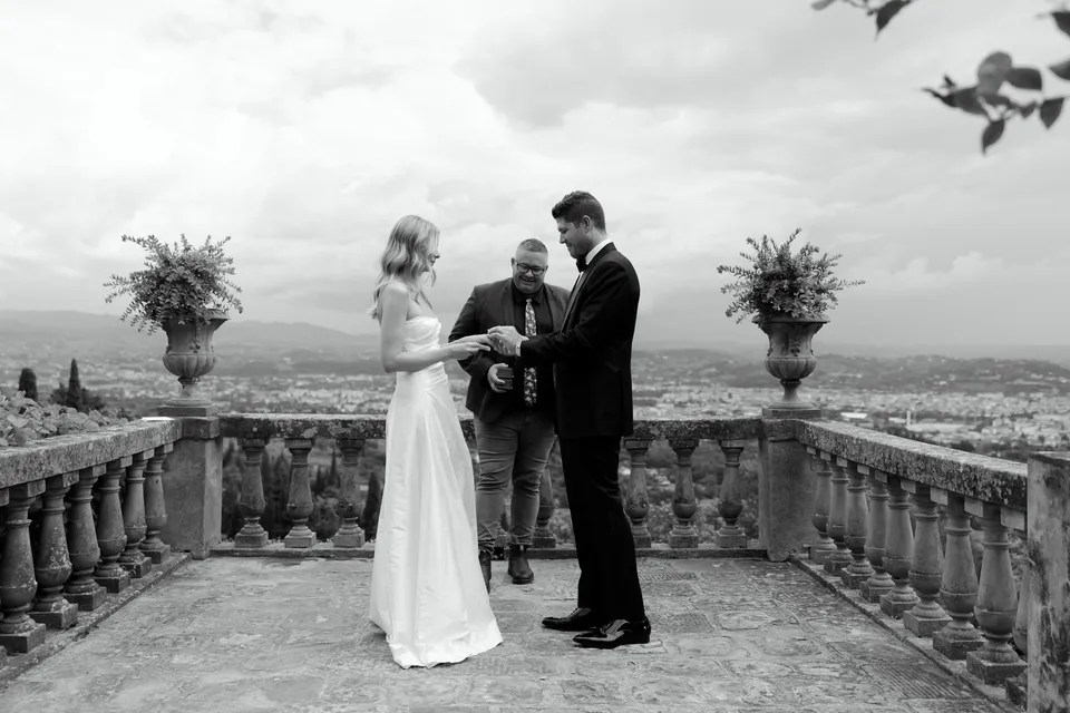 Black-and-white photograph of Holly, Matthew and celebrant Josh Withers together during the terrace ceremony, at Villa San Michele in Fiesole above Florence, Tuscany, Italy, for an Elopement Collective elopement. Digital photograph by Khara from House of Lucie.