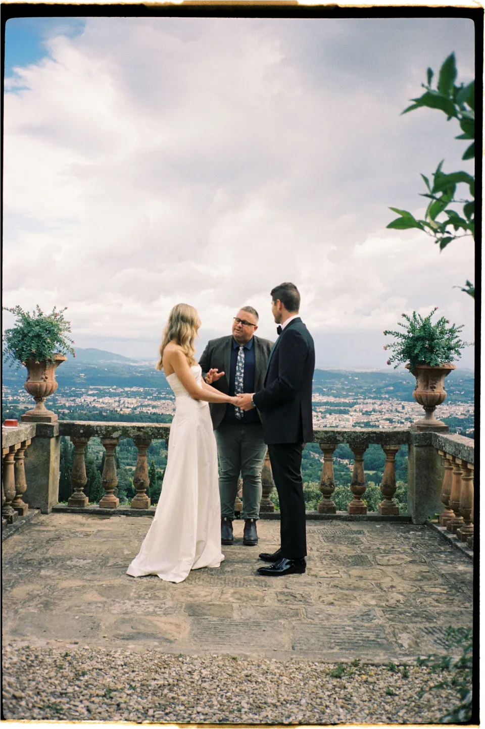 Holly and Matthew holding hands during their ceremony beside the terrace balustrade, at Villa San Michele in Fiesole above Florence, Tuscany, Italy, for an Elopement Collective elopement. Film photograph by Khara from House of Lucie.