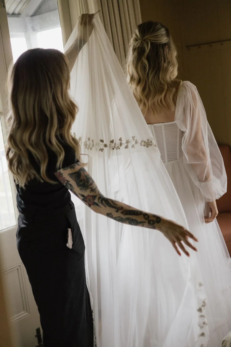 Bridget having the back of her wedding dress fastened beside the cottage window. At Cudgera Creek in northern New South Wales, for an Elopement Collective elopement. Photograph by Bulb Creative.