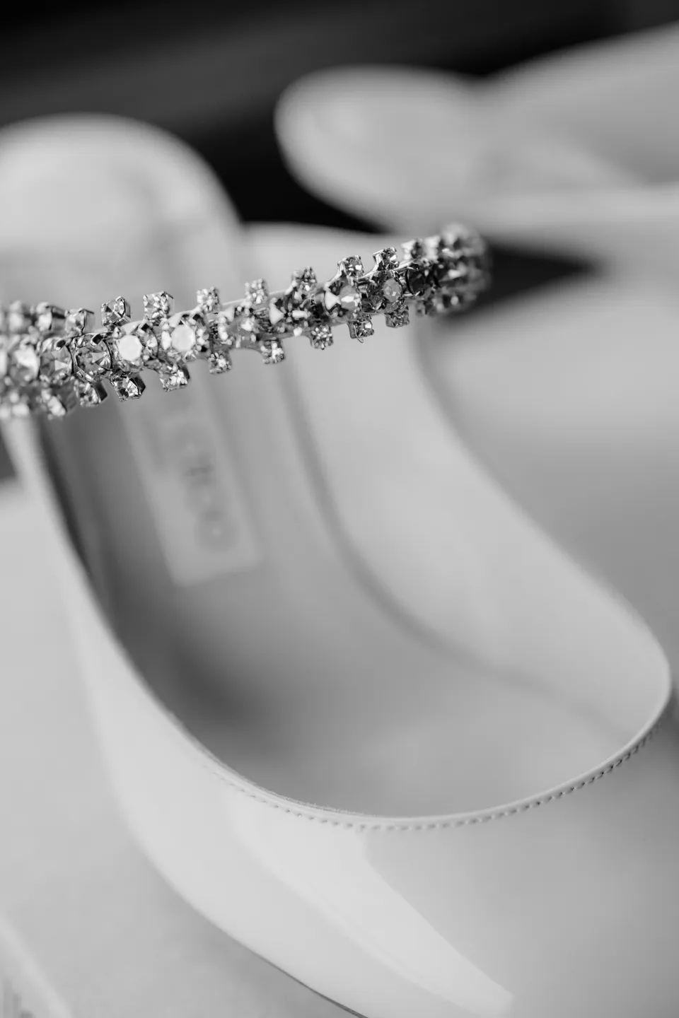 Black and white close-up of a sparkling strap on a white bridal shoe, at Thalia Haven on the East Coast of Tasmania, Australia, for an Elopement Collective elopement. Photograph by Joey Willis.