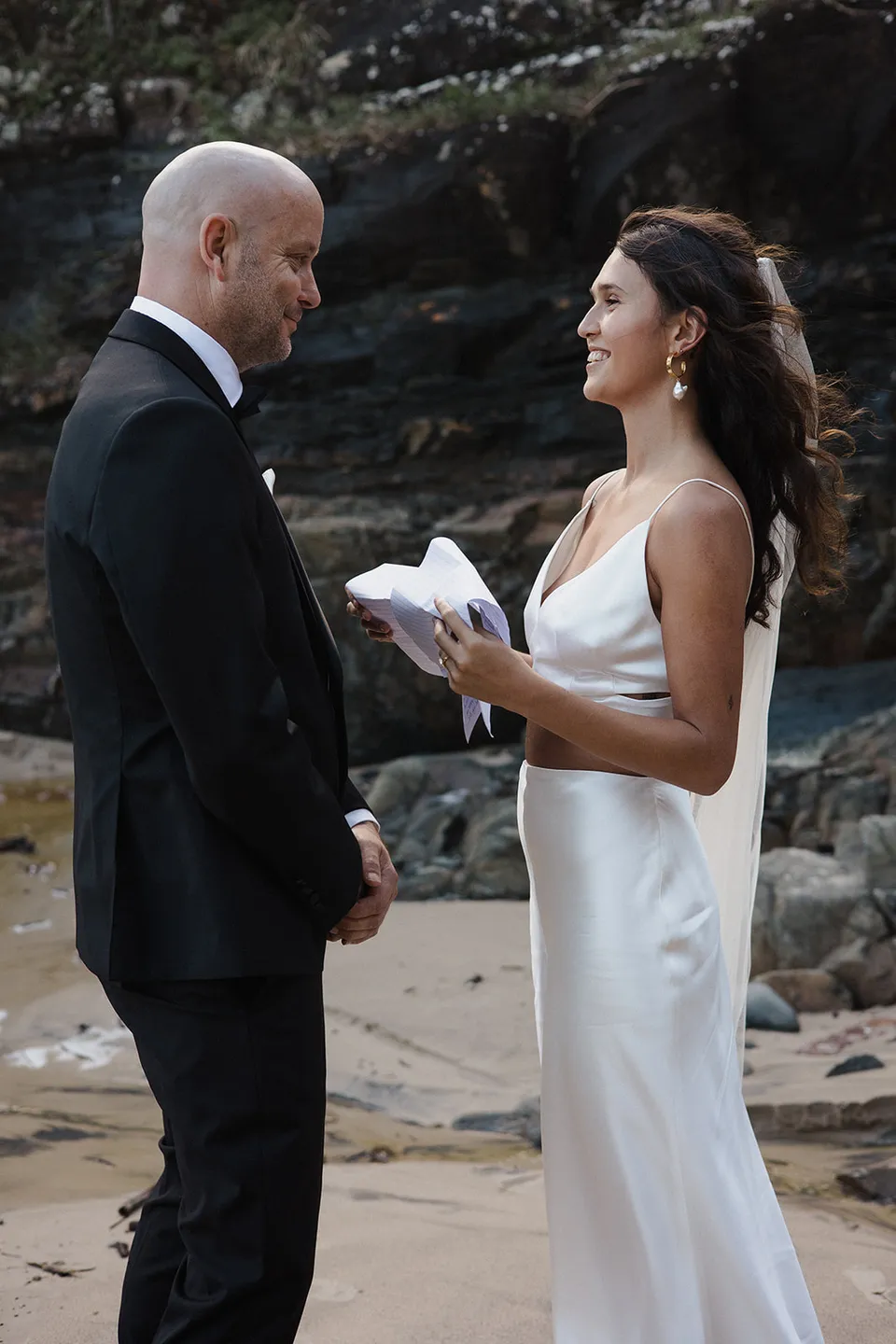 Rachel reading her personal vows to Dane beside the rocks. At Whites Beach, Broken Head, near Byron Bay, for an Elopement Collective elopement. Photograph by Jason Lucas.