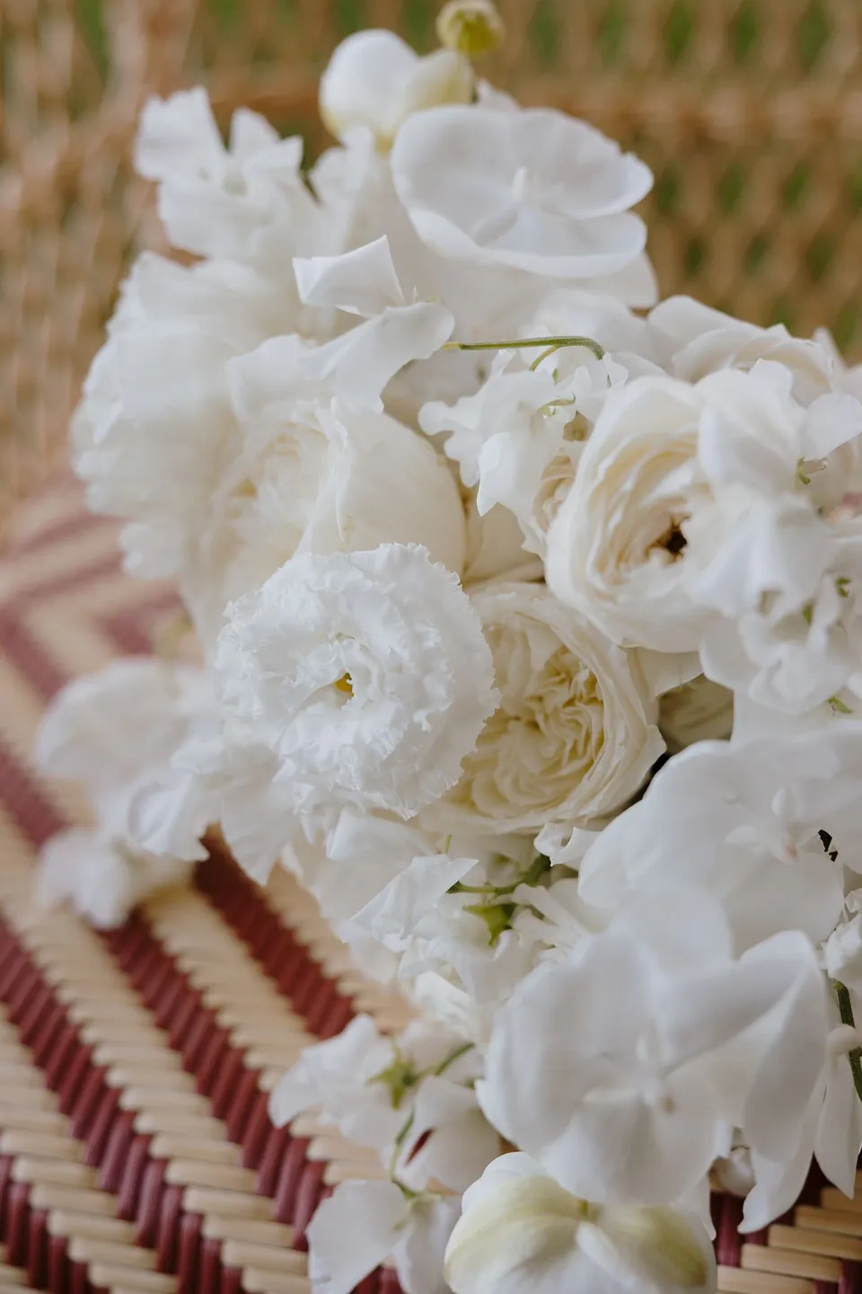 Close view of Zoe’s white orchid and rose bouquet by Garden of Love resting on a woven chair, at Passalacqua in Moltrasio, Lake Como, Italy, for an Elopement Collective elopement. Photo by George Bowden.