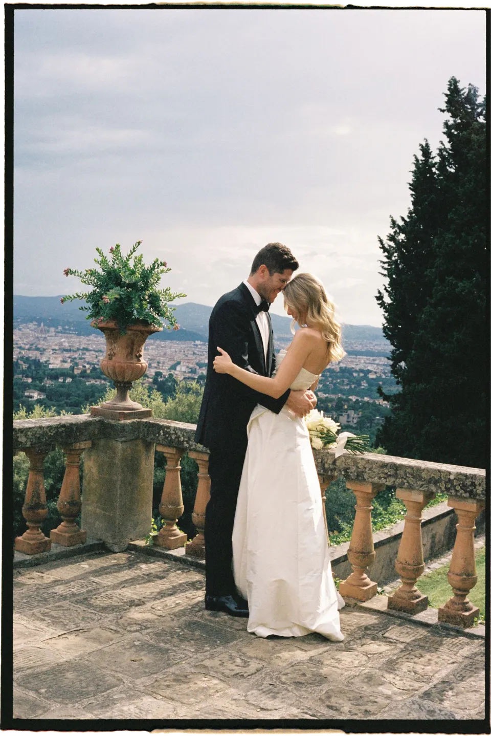 Holly and Matthew embracing and kissing on the terrace above Florence, at Villa San Michele in Fiesole above Florence, Tuscany, Italy, for an Elopement Collective elopement. Film photograph by Khara from House of Lucie.