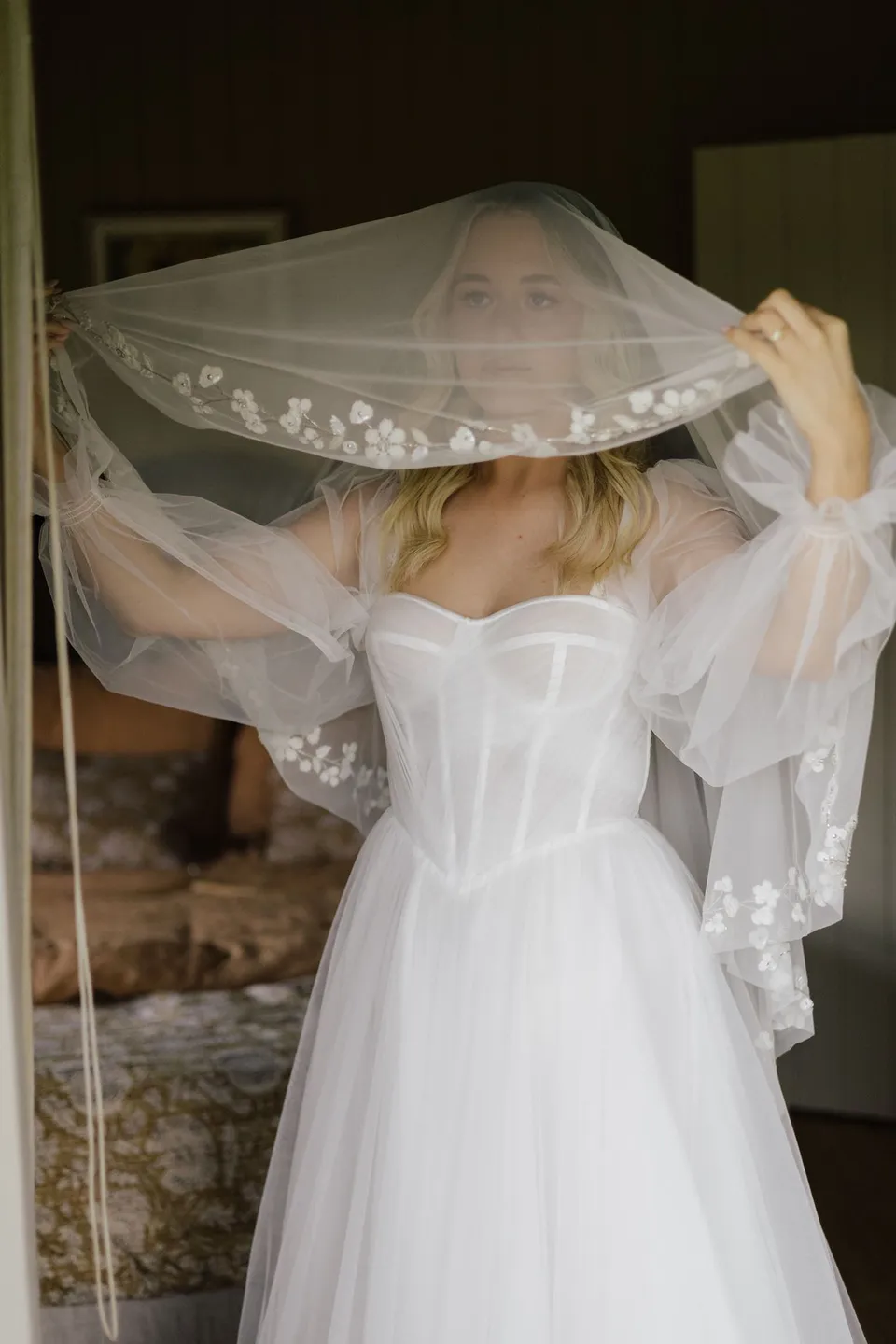 Bridget lifting her embroidered veil over her head as she gets ready. At Cudgera Creek in northern New South Wales, for an Elopement Collective elopement. Photograph by Bulb Creative.
