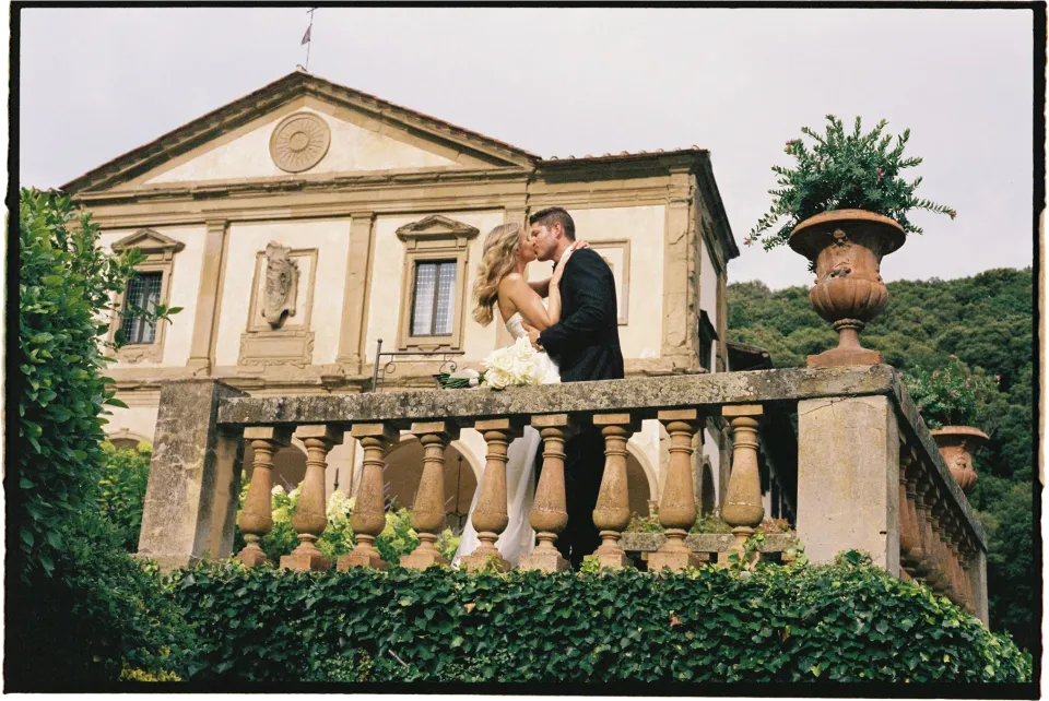 Holly and Matthew kissing beside the balustrade with the villa facade behind them, at Villa San Michele in Fiesole above Florence, Tuscany, Italy, for an Elopement Collective elopement. Film photograph by Khara from House of Lucie.