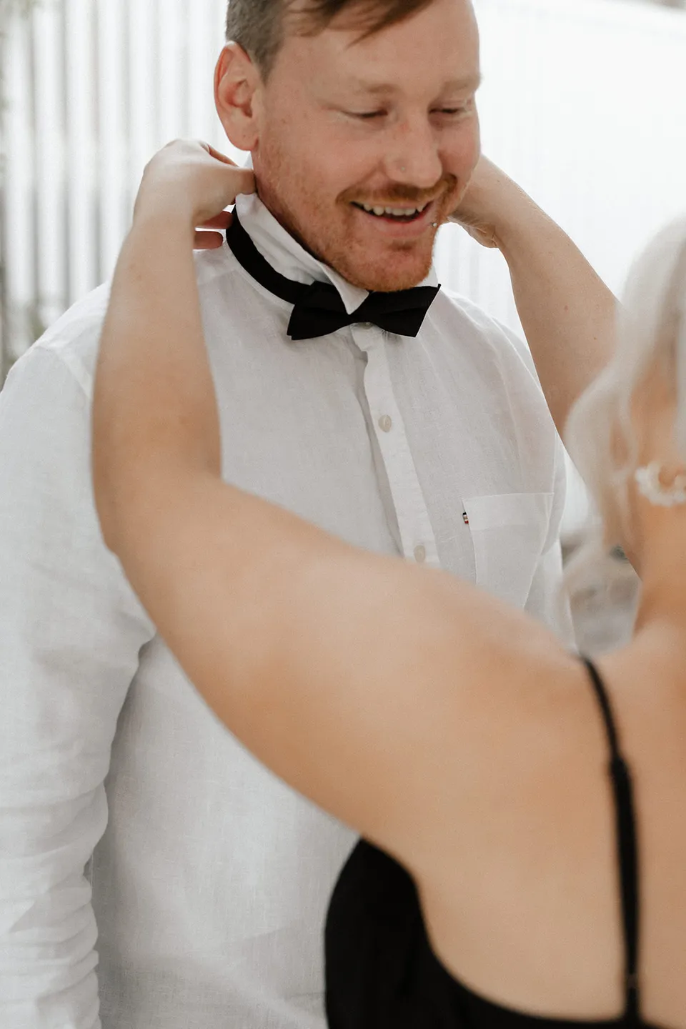 Matt smiling as his black bow tie is adjusted, at Grounds of Cabarita in Cabarita Beach, NSW, for an Elopement Collective elopement. Photo by Bulb Creative.