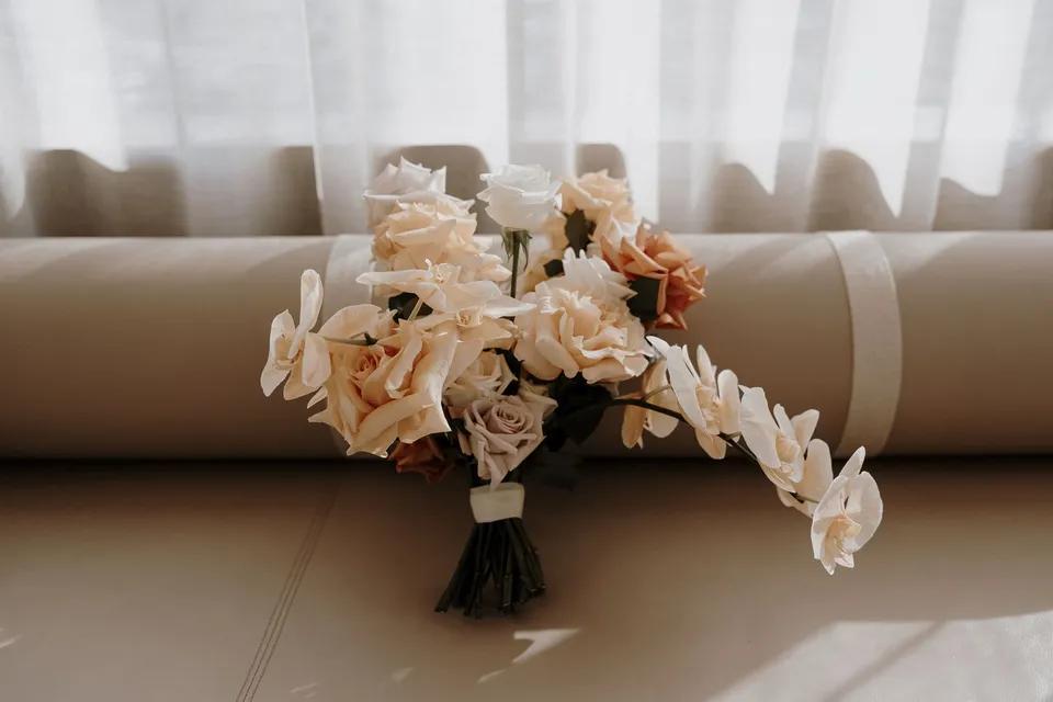 Danielle’s bouquet of peach and white flowers with trailing orchids resting on a pale sofa, during Danielle and Adam’s Elopement Collective elopement at The Calile Hotel in Fortitude Valley, Brisbane.