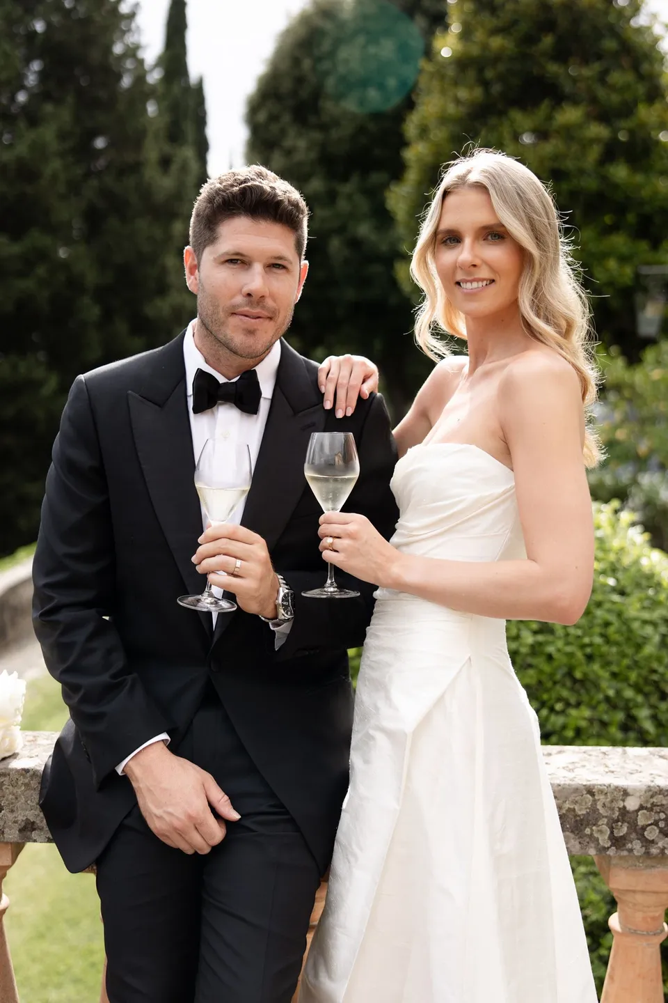 Holly and Matthew standing together with glasses of wine against the garden greenery, at Villa San Michele in Fiesole above Florence, Tuscany, Italy, for an Elopement Collective elopement. Digital photograph by Khara from House of Lucie.