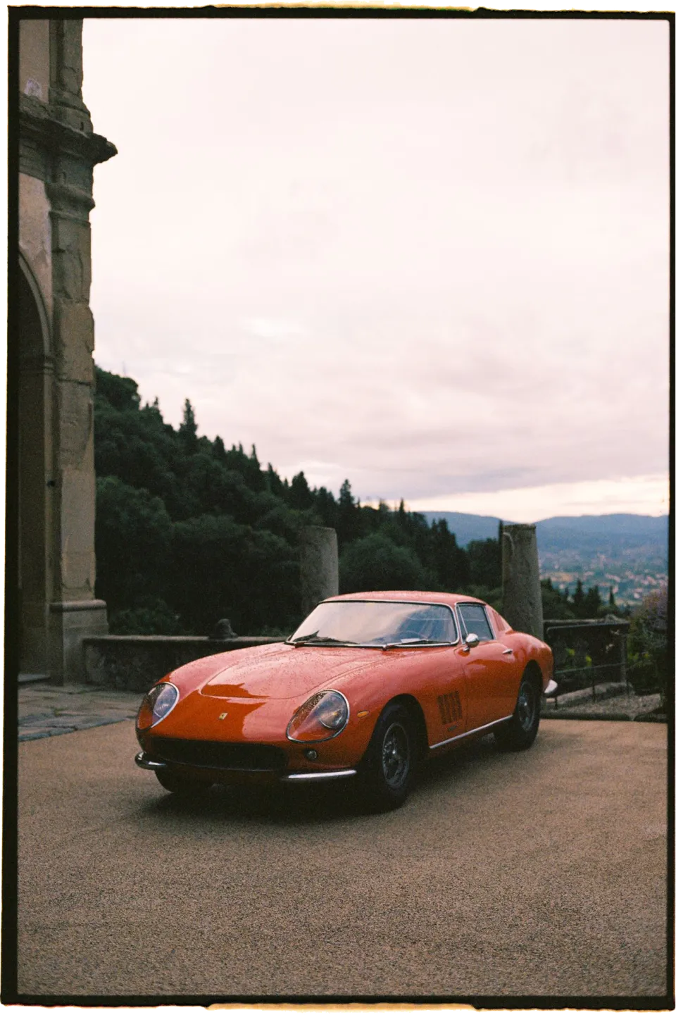 A red vintage sports car parked beside the villa’s stone arches under a cloudy sky, at Villa San Michele in Fiesole above Florence, Tuscany, Italy, for an Elopement Collective elopement. Film photograph by Khara from House of Lucie.