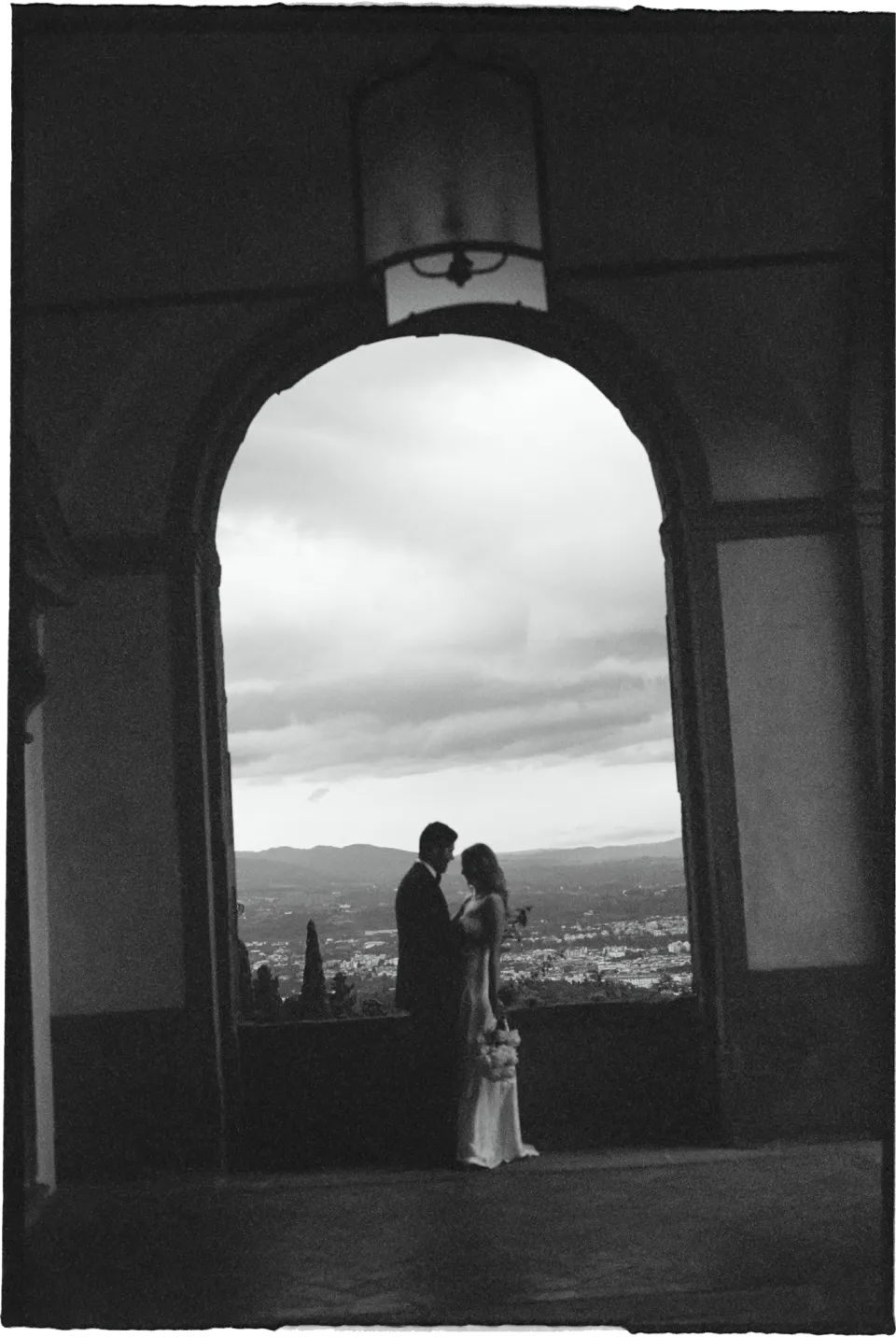 Black-and-white photograph of Holly and Matthew together beneath a stone arch overlooking Florence, at Villa San Michele in Fiesole above Florence, Tuscany, Italy, for an Elopement Collective elopement. Film photograph by Khara from House of Lucie.