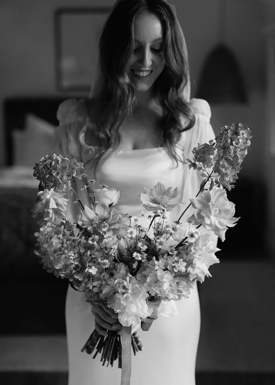 Black-and-white portrait of Elyse looking down at her bouquet, with flowers by The Perfect Party Co. At Fig Tree Villa in Ewingsdale, Byron Bay, for an Elopement Collective elopement. Photograph by Bulb Creative.