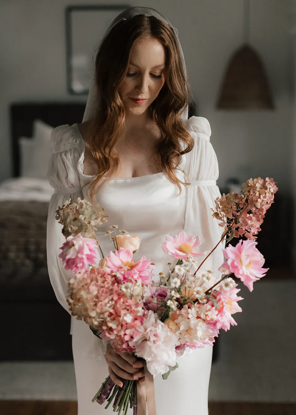 Elyse smiling softly at her pink and cream bouquet, with flowers by The Perfect Party Co. At Fig Tree Villa in Ewingsdale, Byron Bay, for an Elopement Collective elopement. Photograph by Bulb Creative.