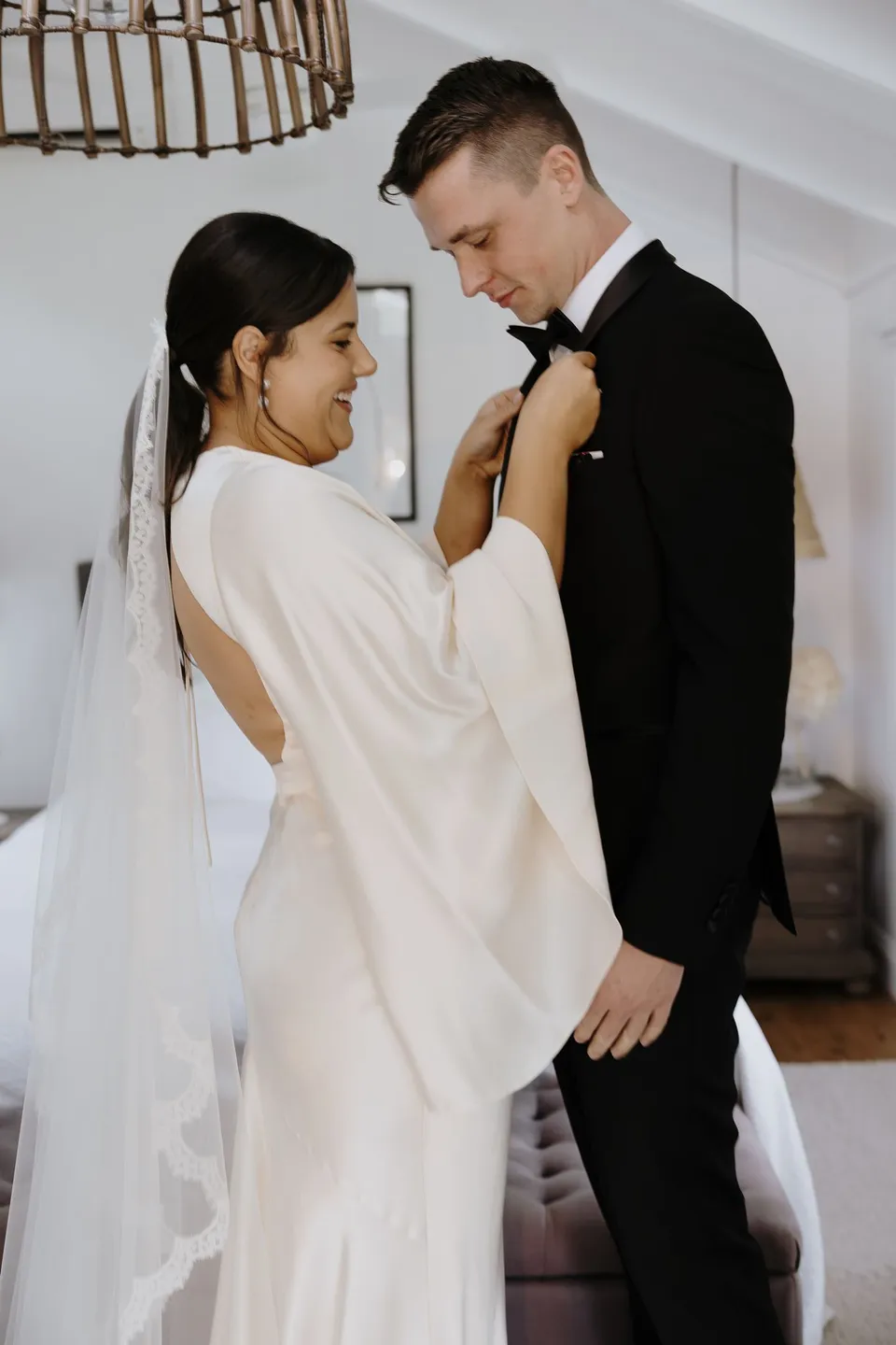Laura adjusting Matthew's bow tie while they get ready together. At Fig Tree Villa in Ewingsdale, Byron Bay, for an Elopement Collective elopement. Photograph by George Bowden.