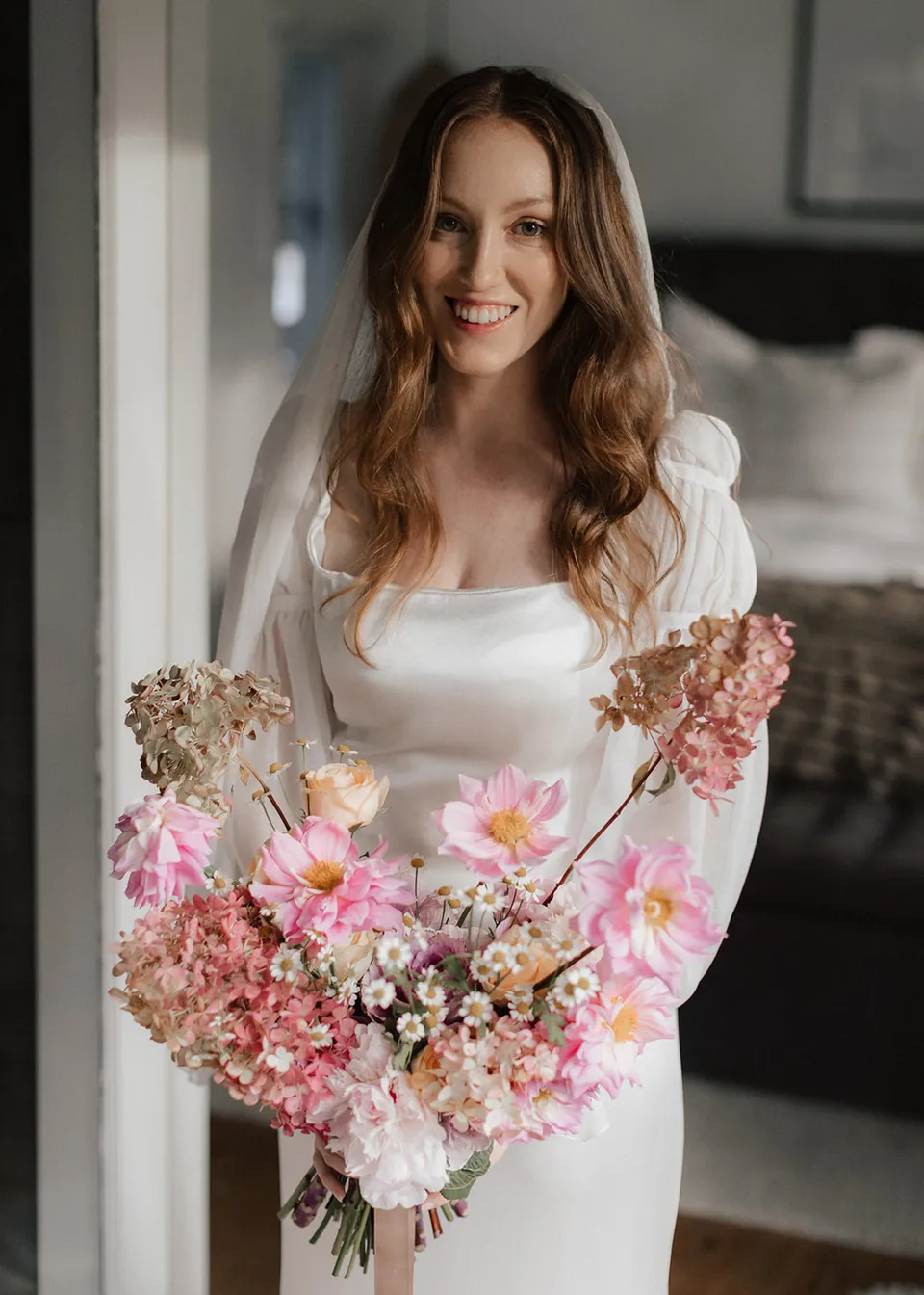 Elyse smiling towards the camera with her colourful bouquet, with flowers by The Perfect Party Co. At Fig Tree Villa in Ewingsdale, Byron Bay, for an Elopement Collective elopement. Photograph by Bulb Creative.