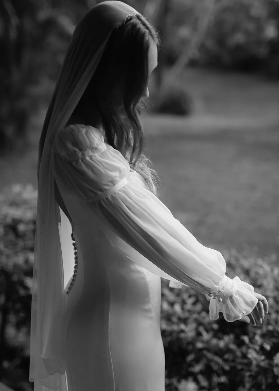 Black-and-white side portrait of Elyse adjusting her sheer dress sleeve outdoors. At Fig Tree Villa in Ewingsdale, Byron Bay, for an Elopement Collective elopement. Photograph by Bulb Creative.