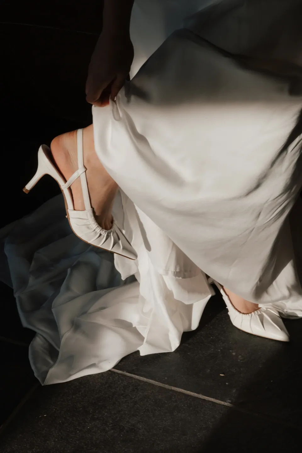 Dani lifting the hem of her dress while fastening a white slingback shoe, at Thalia Haven on Tasmania’s east coast, for an Elopement Collective elopement. Photograph by Bulb Creative.