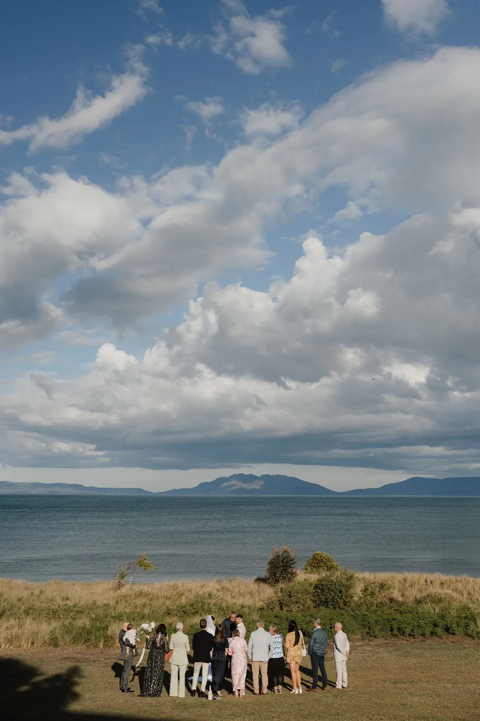 Renee and Mitch’s small ceremony gathering beside Great Oyster Bay, beneath a broad sky of blue and cloud. At Piermont Retreat on Tasmania’s east coast, for an Elopement Collective elopement. Photograph by Bulb Creative.