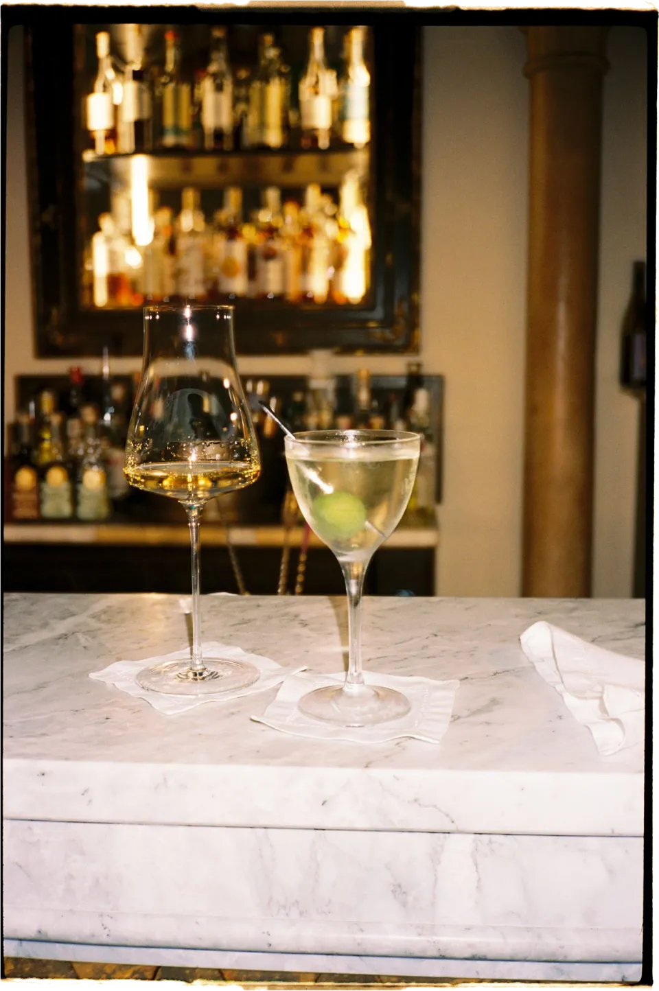 Two glasses of white wine on the marble counter in front of the villa bar, at Villa San Michele in Fiesole above Florence, Tuscany, Italy, for an Elopement Collective elopement. Film photograph by Khara from House of Lucie.