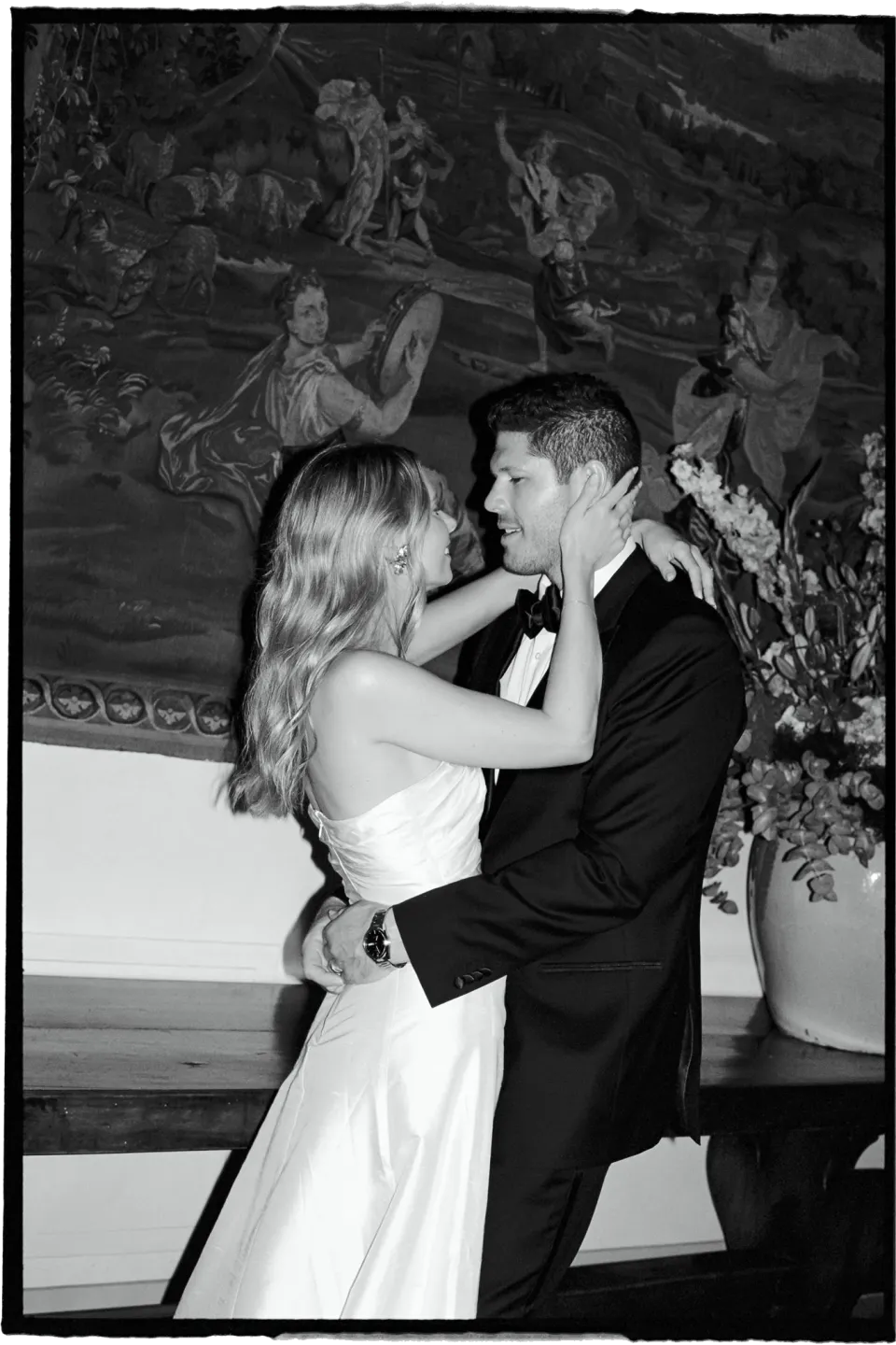 Black-and-white photograph of Holly and Matthew embracing in front of a large tapestry, at Villa San Michele in Fiesole above Florence, Tuscany, Italy, for an Elopement Collective elopement. Film photograph by Khara from House of Lucie.