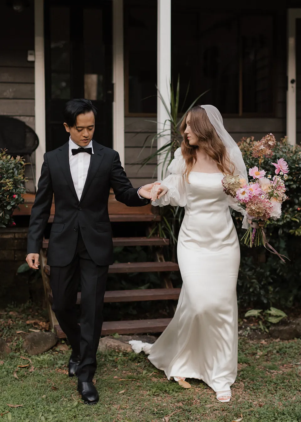 Elyse and Jonathan holding hands as they leave the cottage steps. At Fig Tree Villa in Ewingsdale, Byron Bay, for an Elopement Collective elopement. Photograph by Bulb Creative.